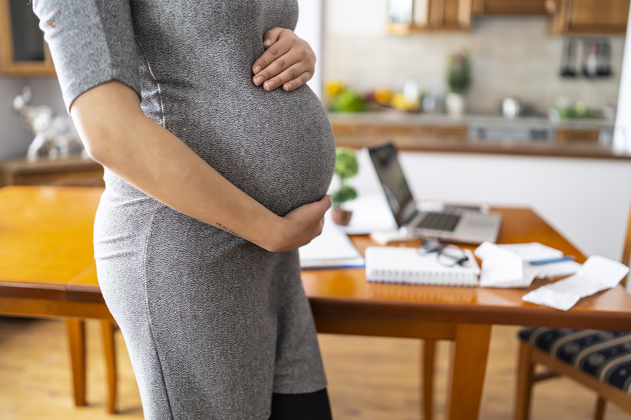 pregnant woman standing at home, hands on belly