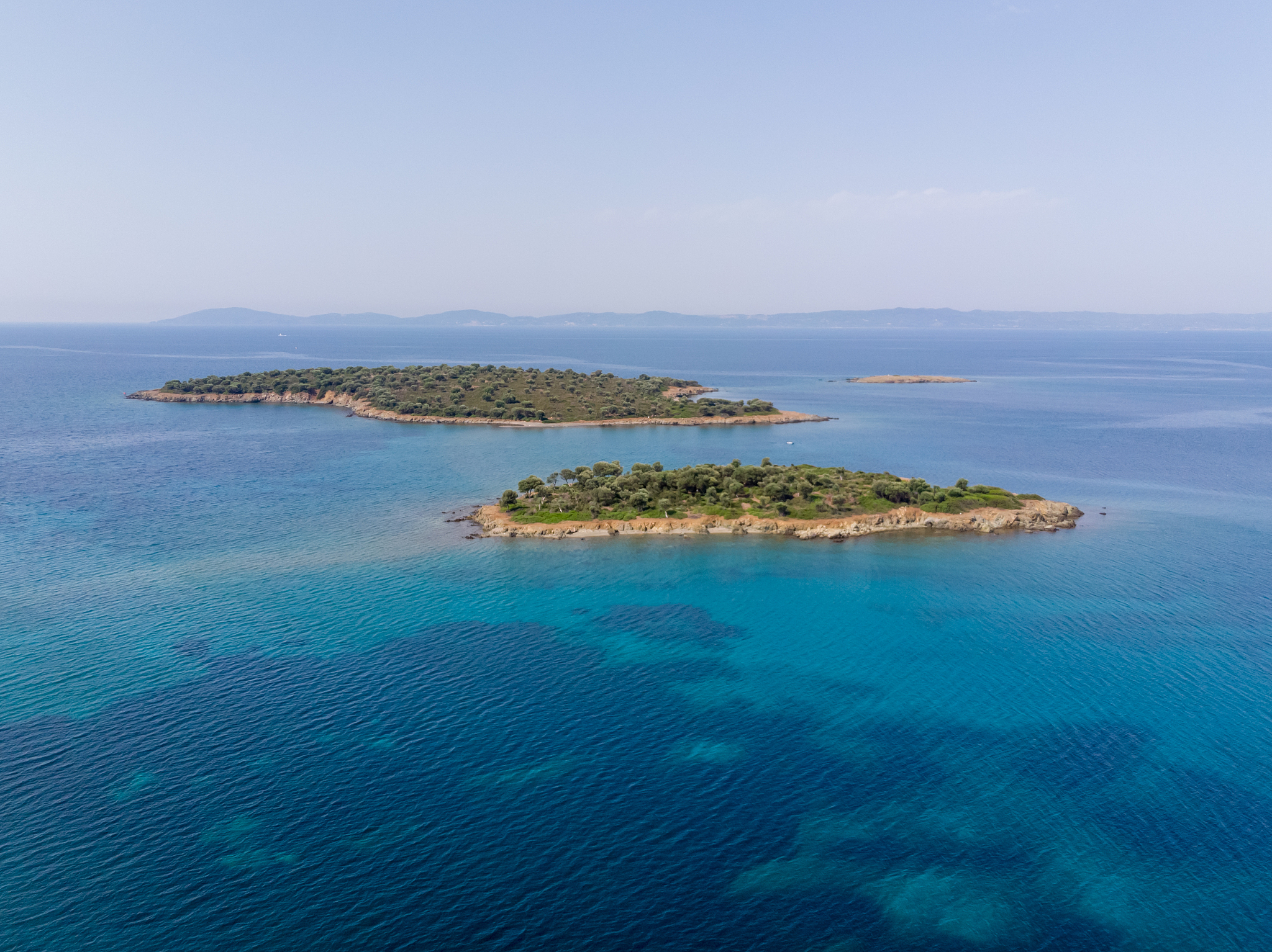 two small islands surrounded with blue sea water with mountains 