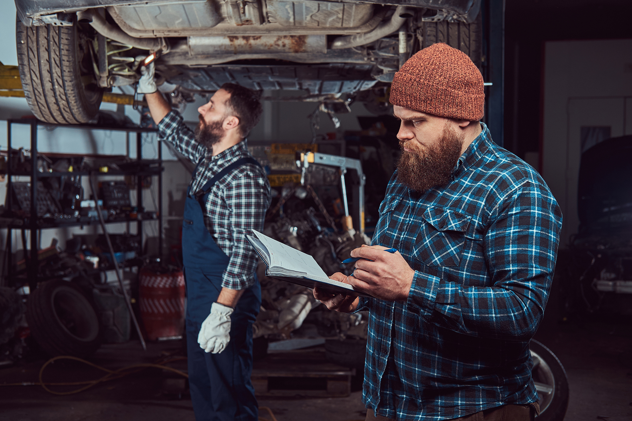 two bearded brutal mechanics repair a car on a lift in the garag