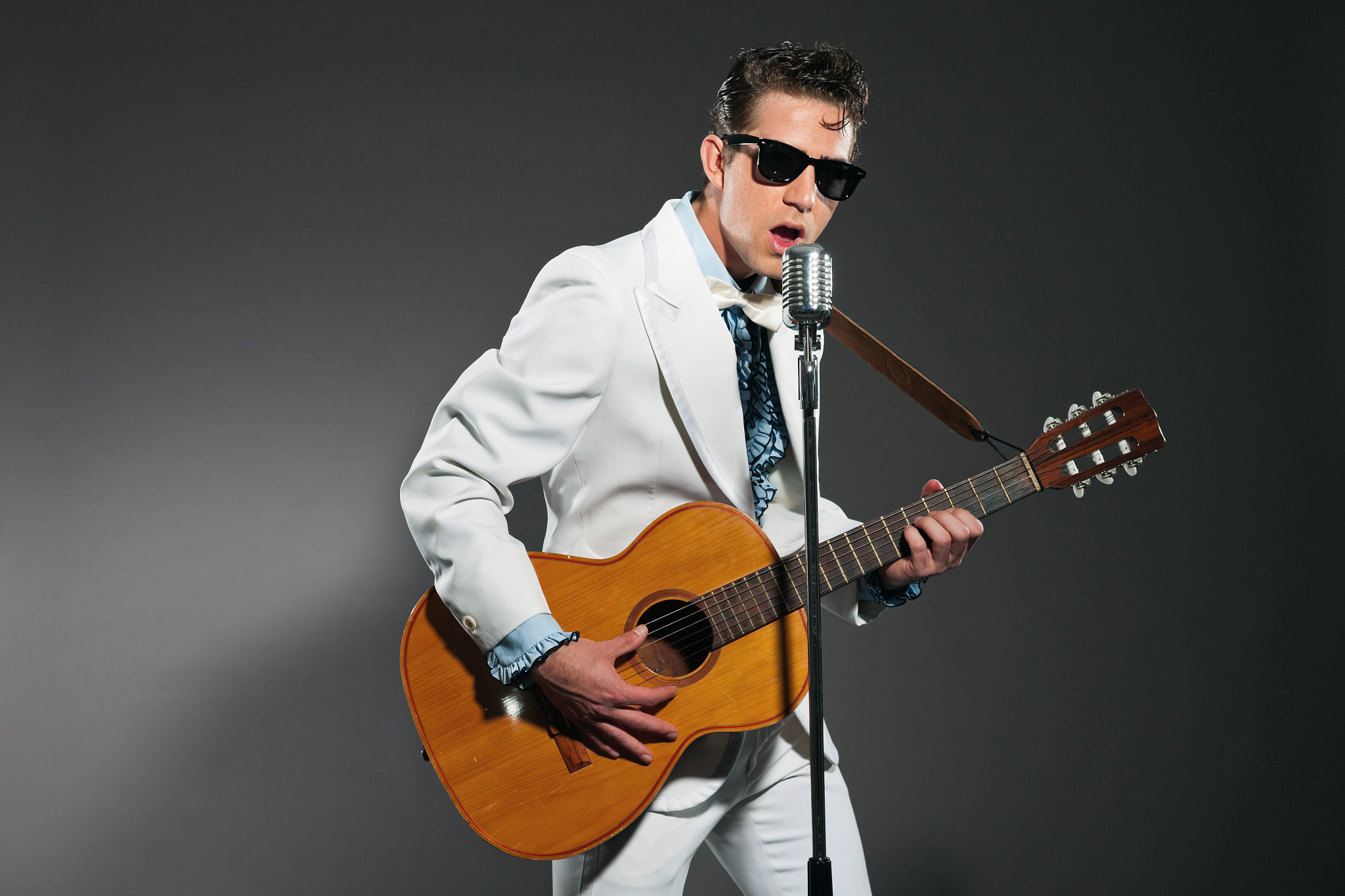 retro rock and roll singer with guitar wearing white suit.