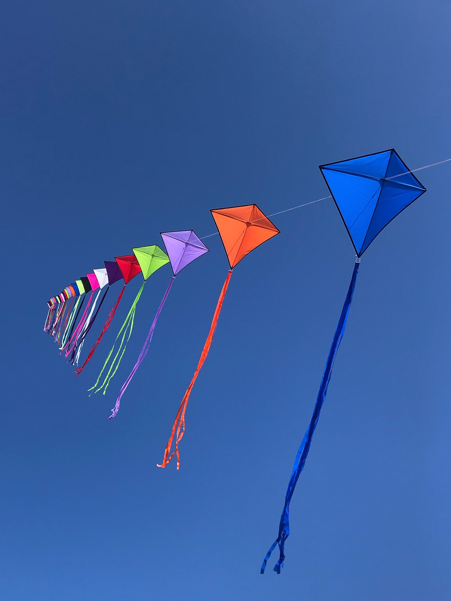 low angle view of multi colored kites flying against clear blue 
