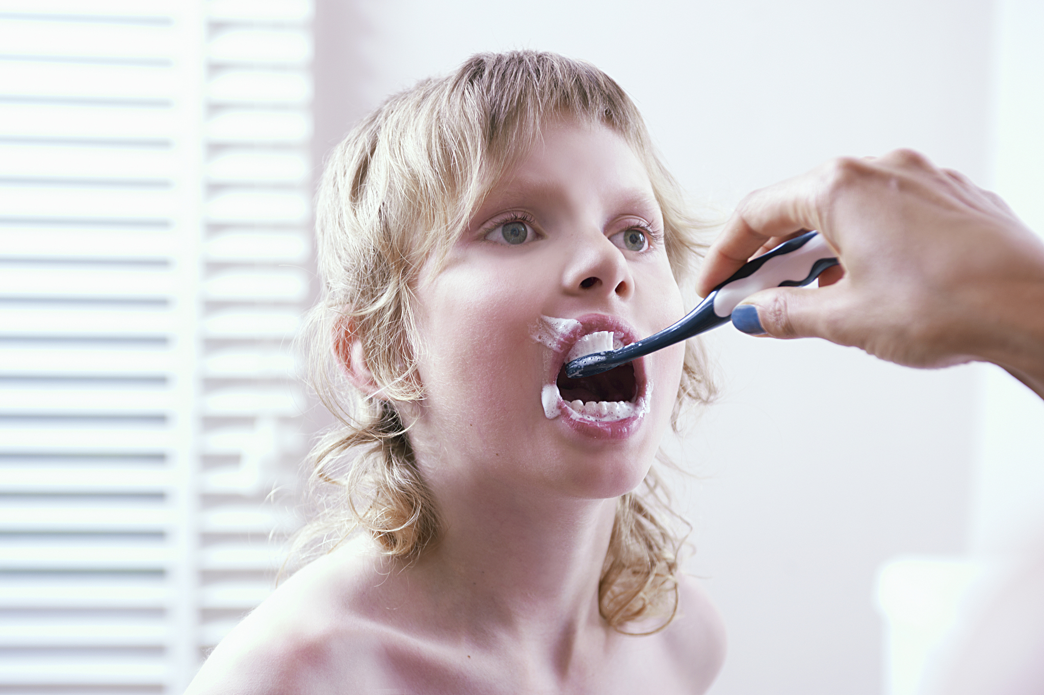 boy getting teeth brushed by mother
