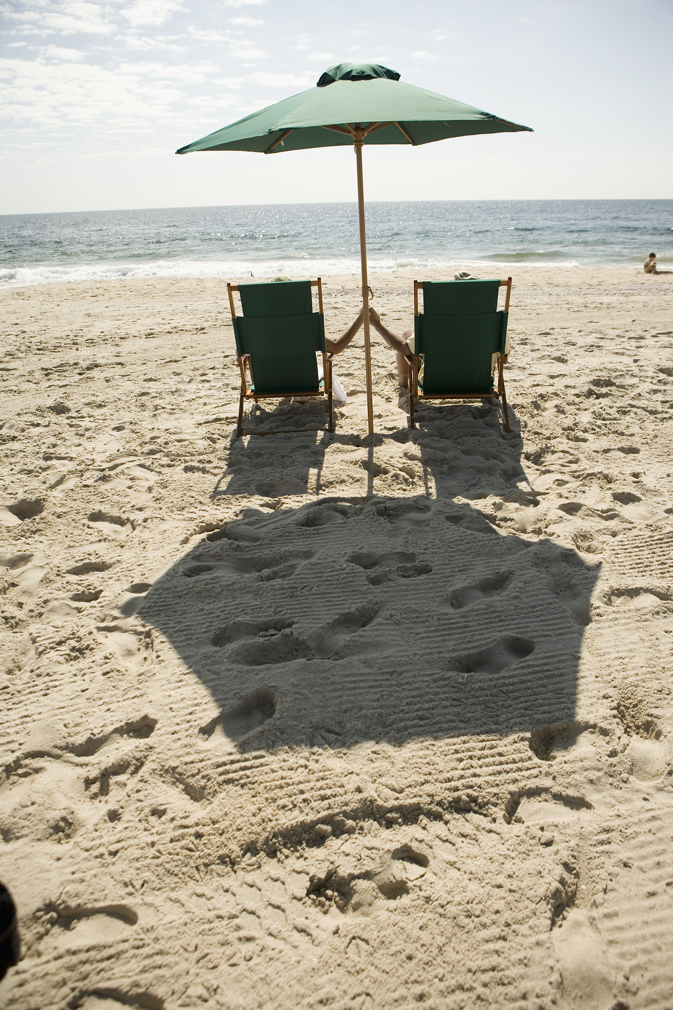 couple relaxing in beach chairs, holding hands, rear view