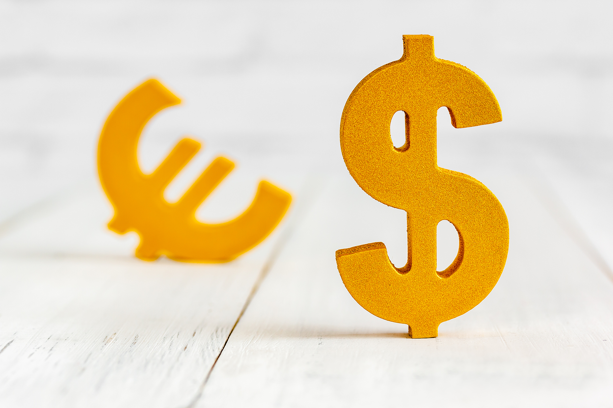 dollar sign over euro sign on white wood table over white brick 