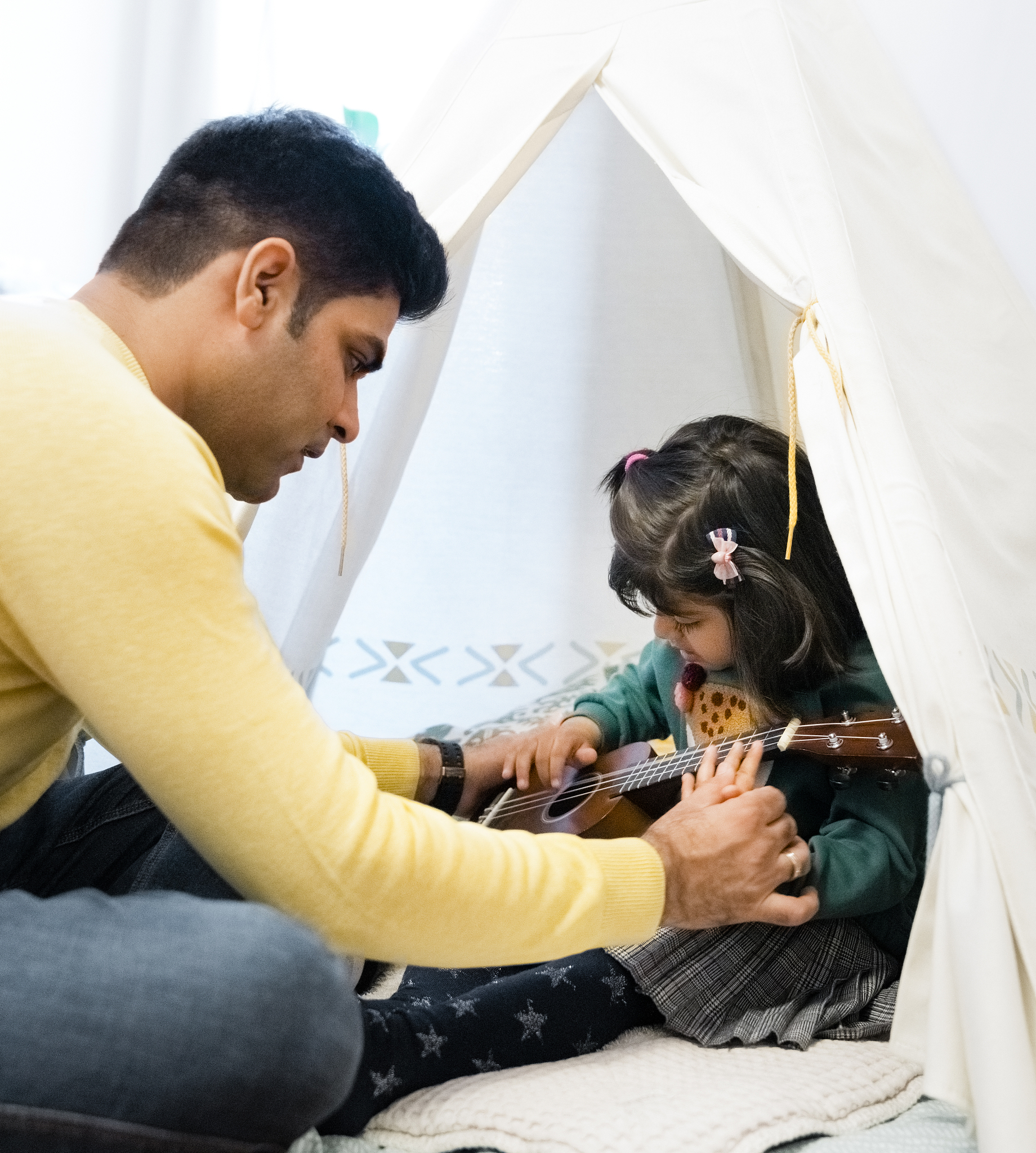 man teaching daughter playing ukelele in tent