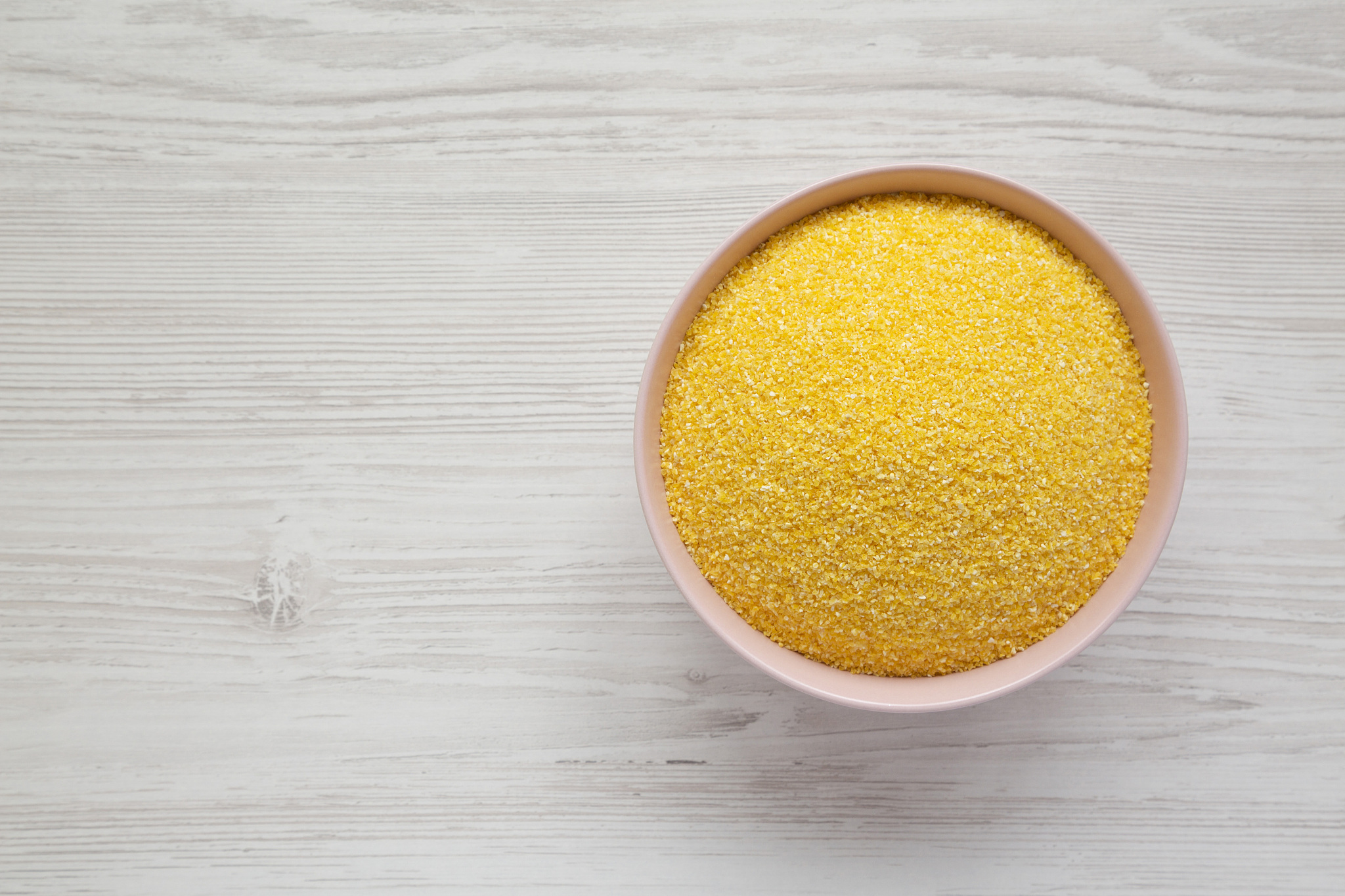 organic masarepa corn meal in a pink bowl over white wooden back