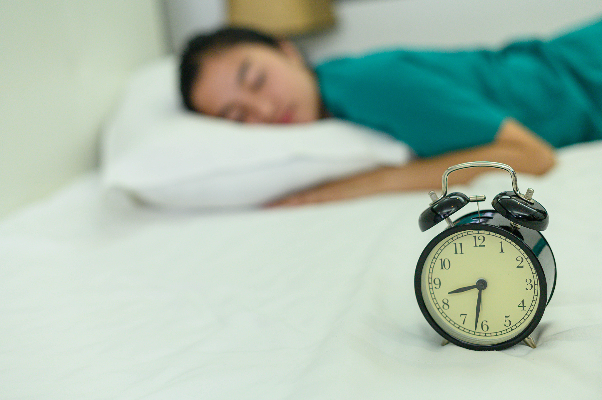 sleeping girl on a white bed beside an alarm clock.