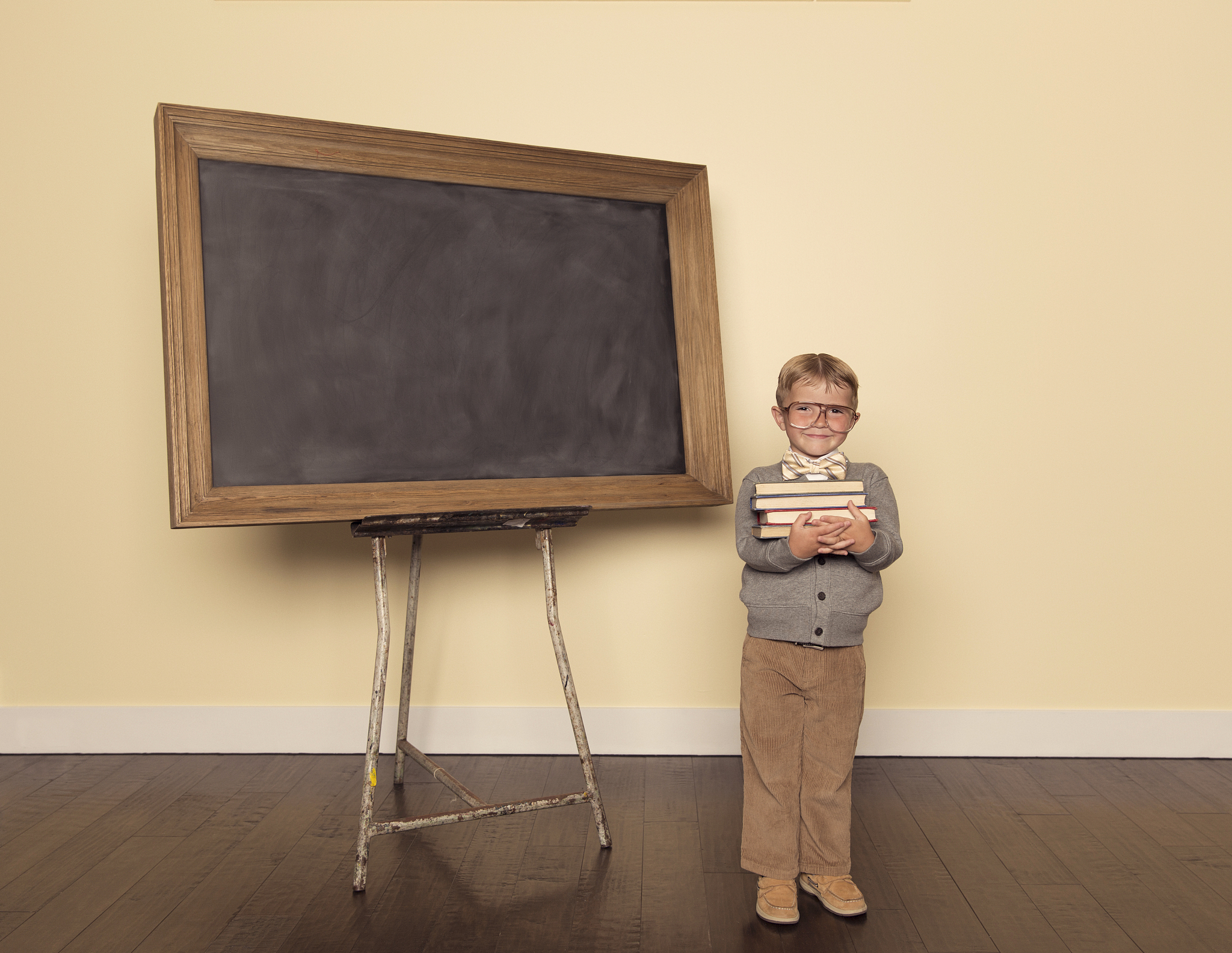 young boy dressed as nerd at chalkboard holding books