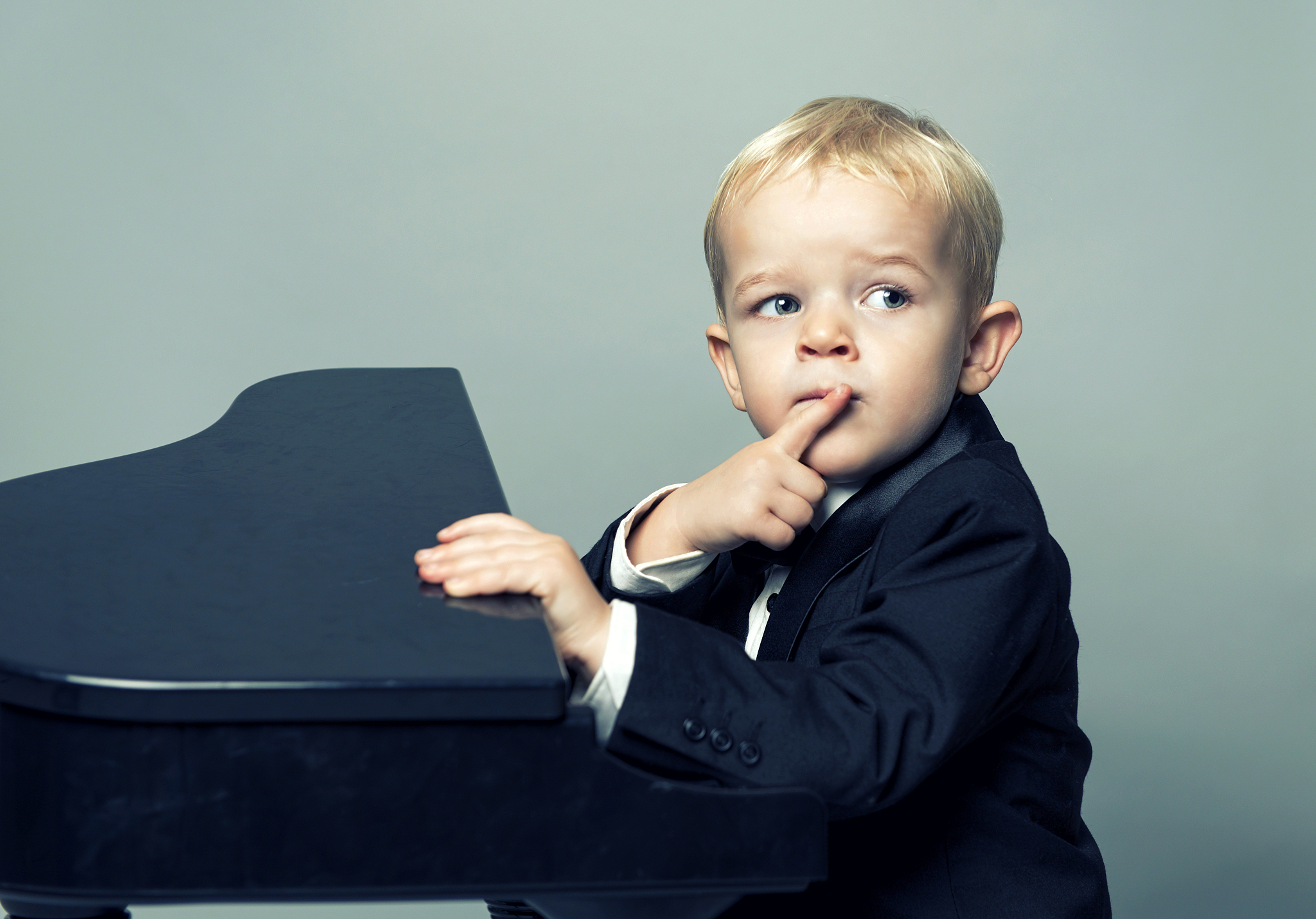 boy with tuxedo sits in front of piano thinking