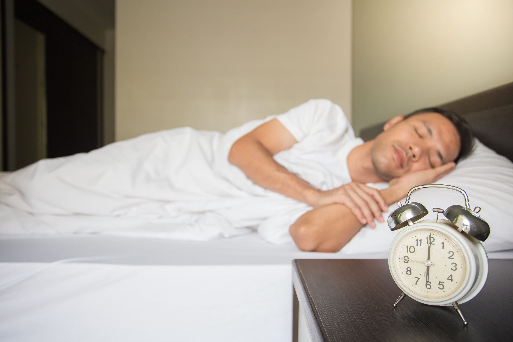 man sleeping on bed by alarm clock at night table in bedroom