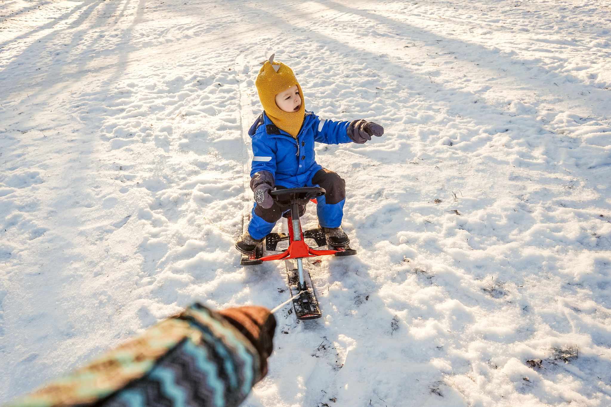 woman rolls child on snowmobile in park.
