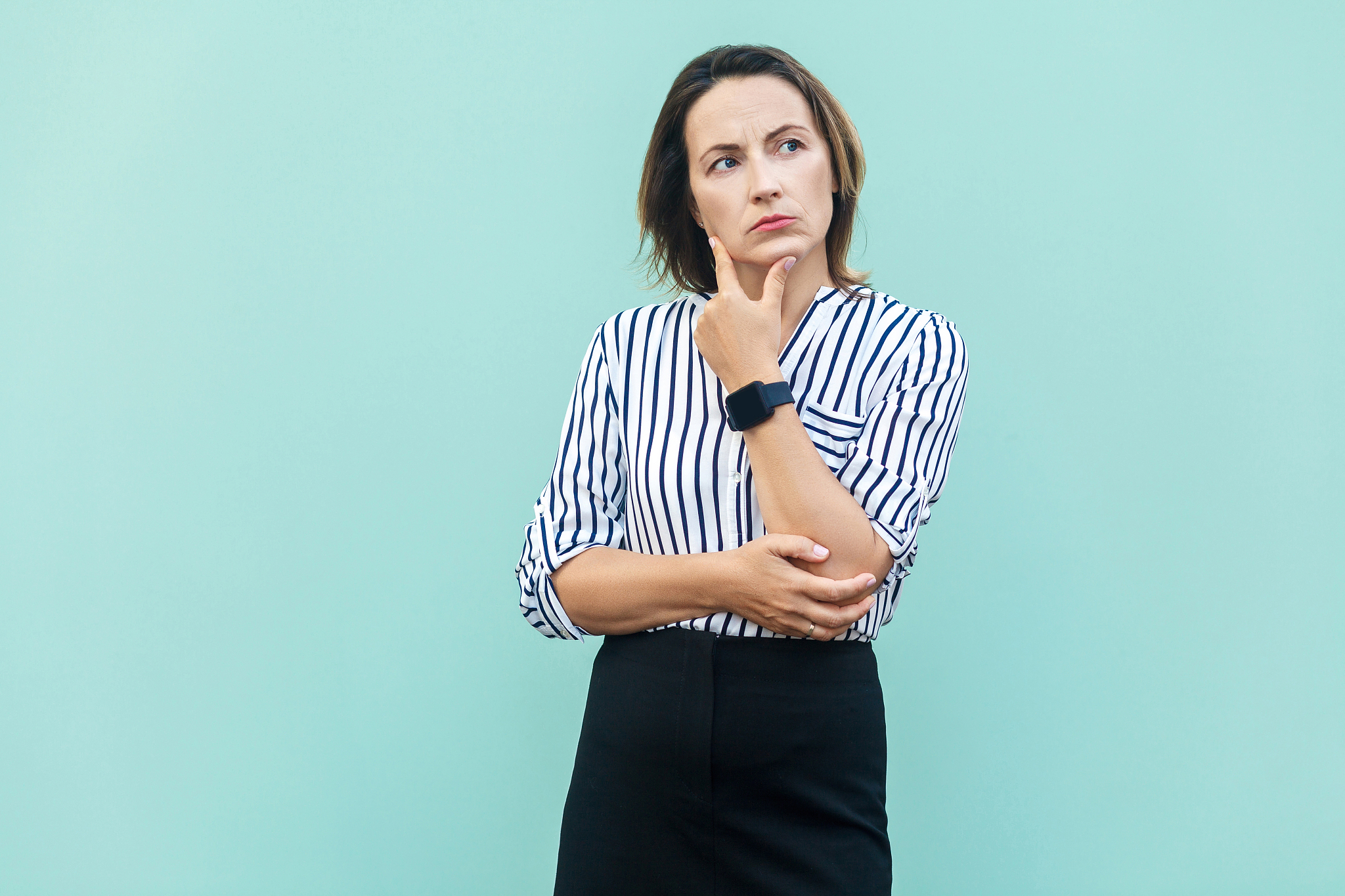 thoughtful business woman looking away while standing against li