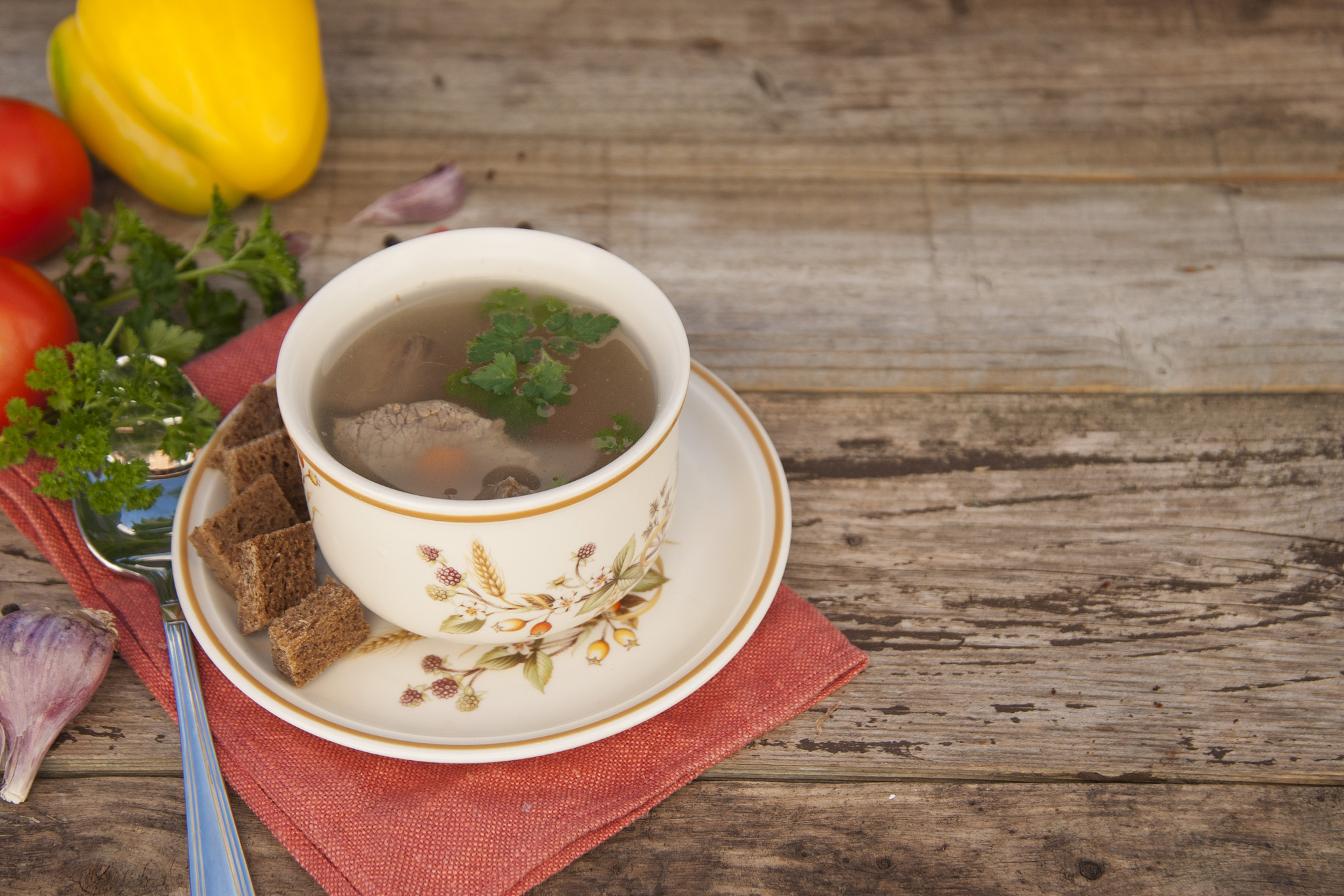 clear beef broth, bouillon in white bowl and vegetables on woode
