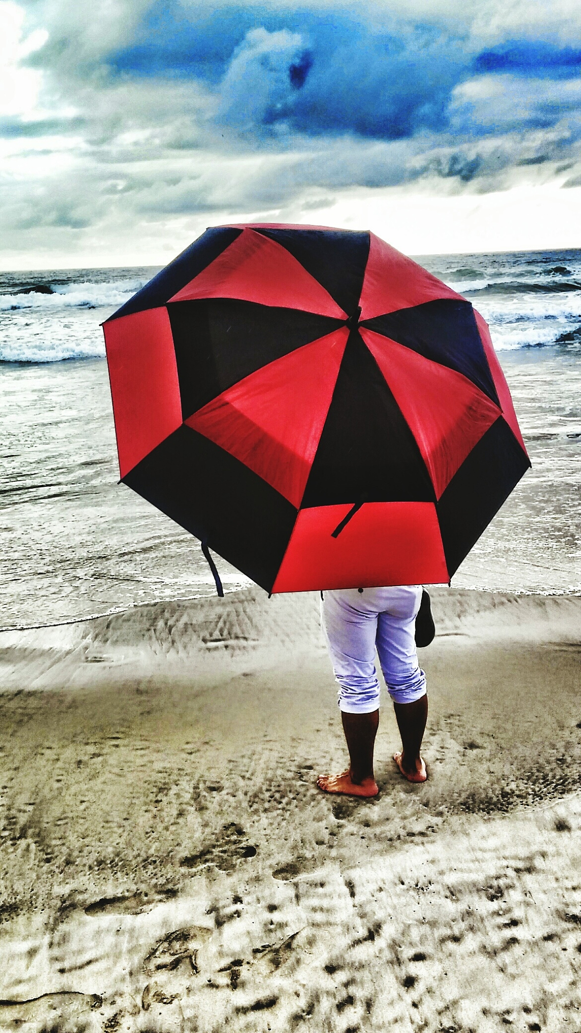 low section of person with umbrella on shore at beach against sk