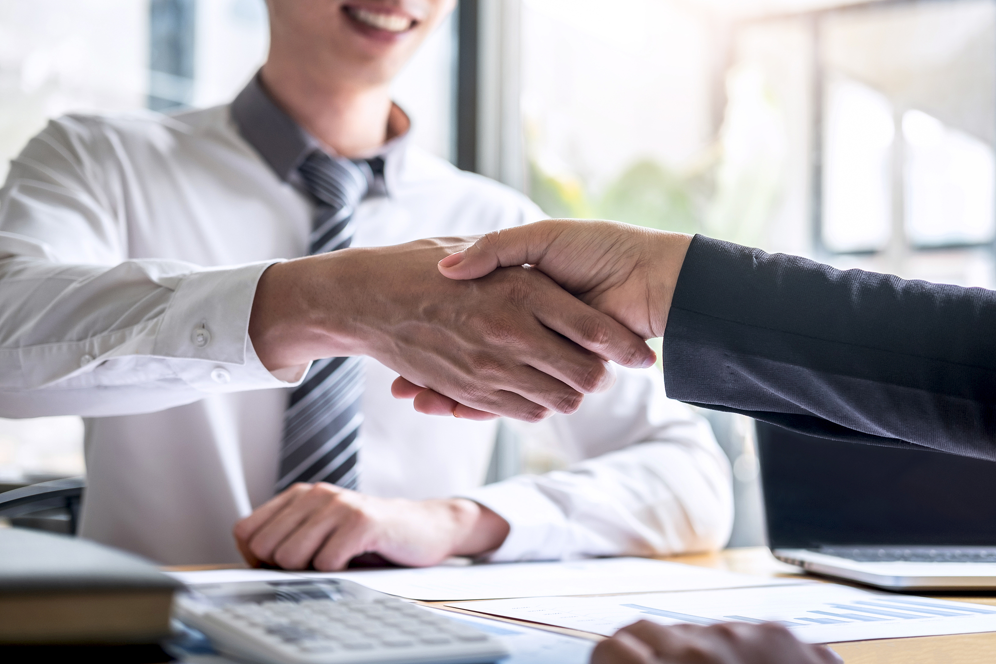 midsection of businessman and colleague shaking hands on table