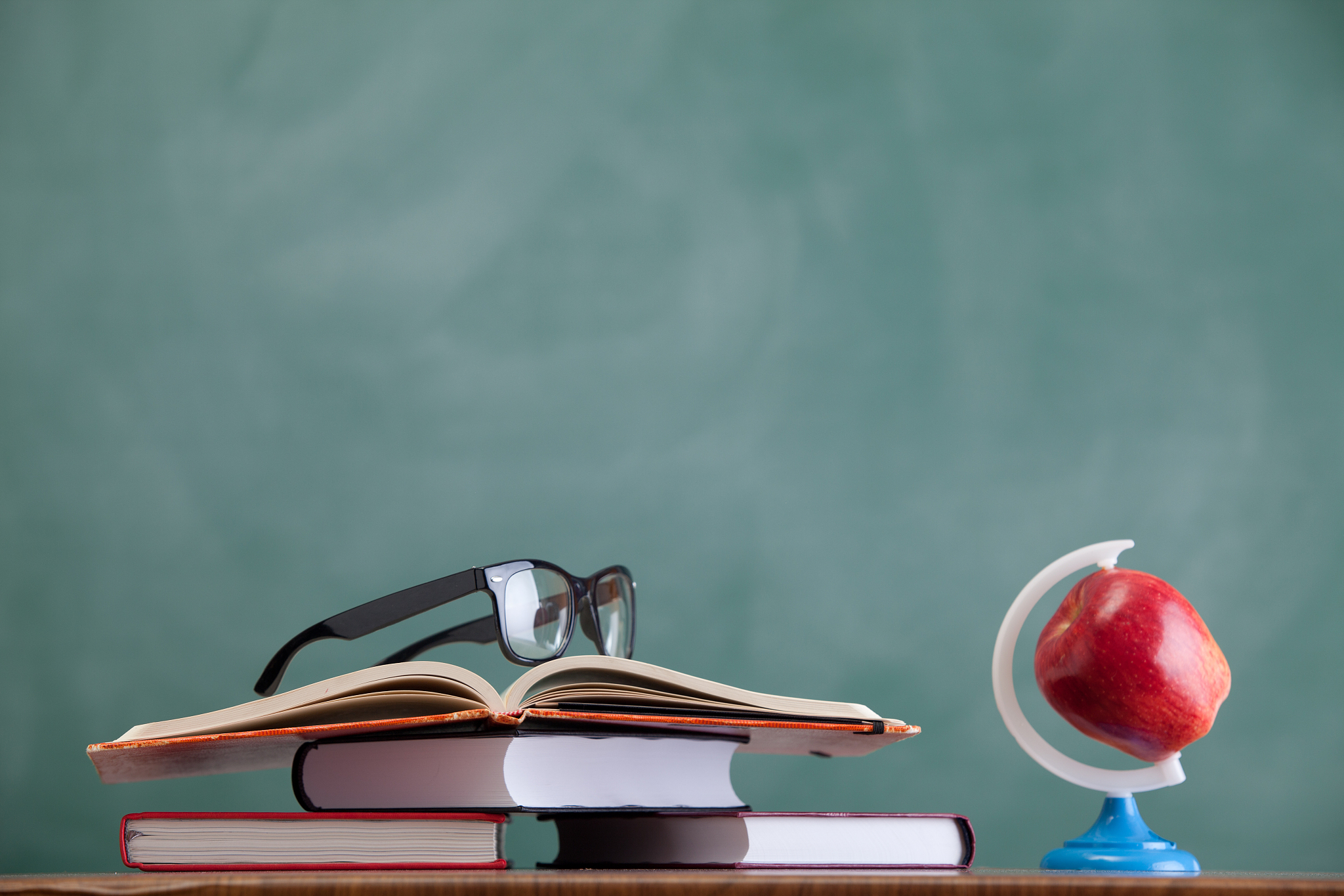glass, apple and stack of books before blackboard