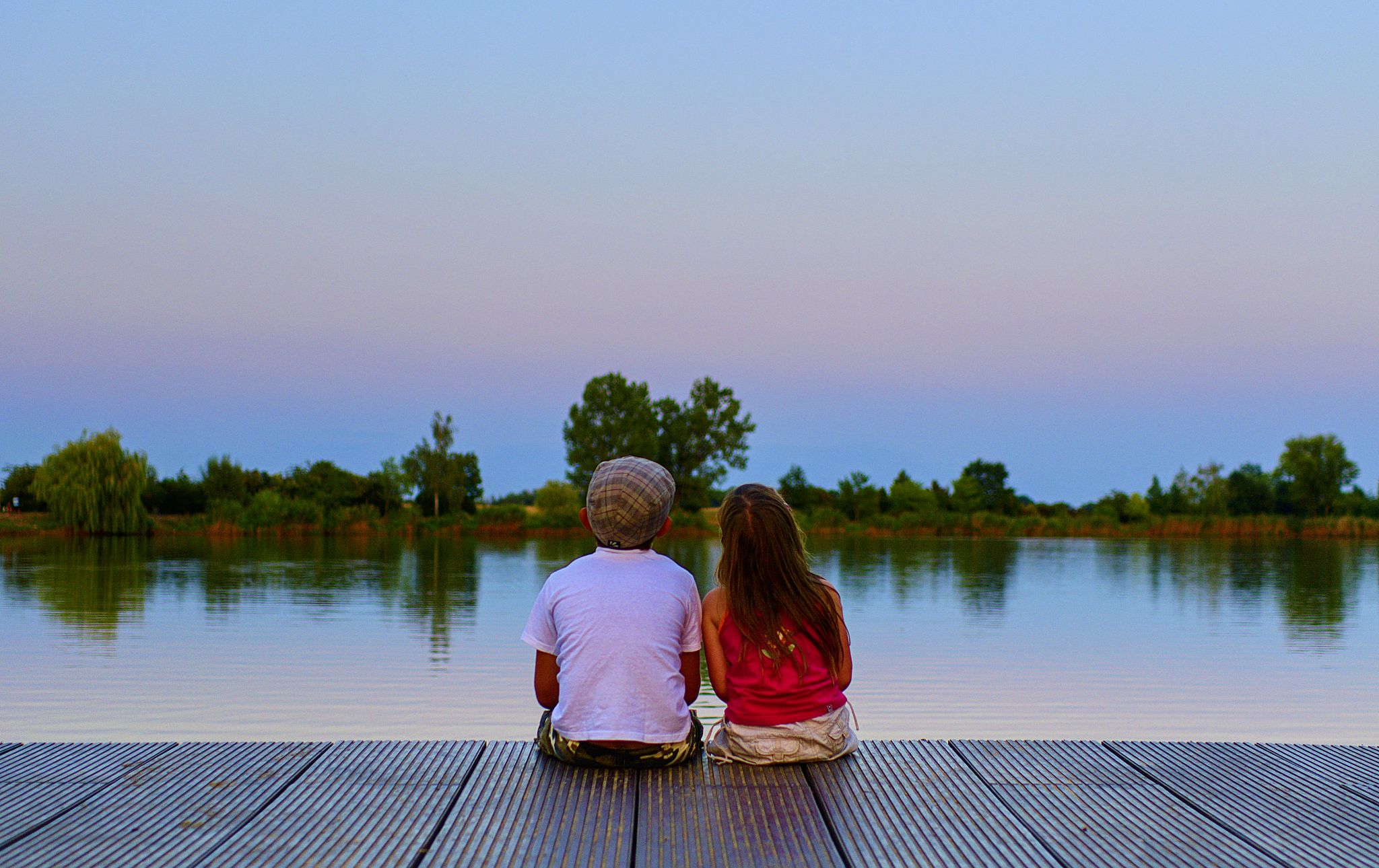 boy with flat cap and little girl are sitting on pier. boy and g