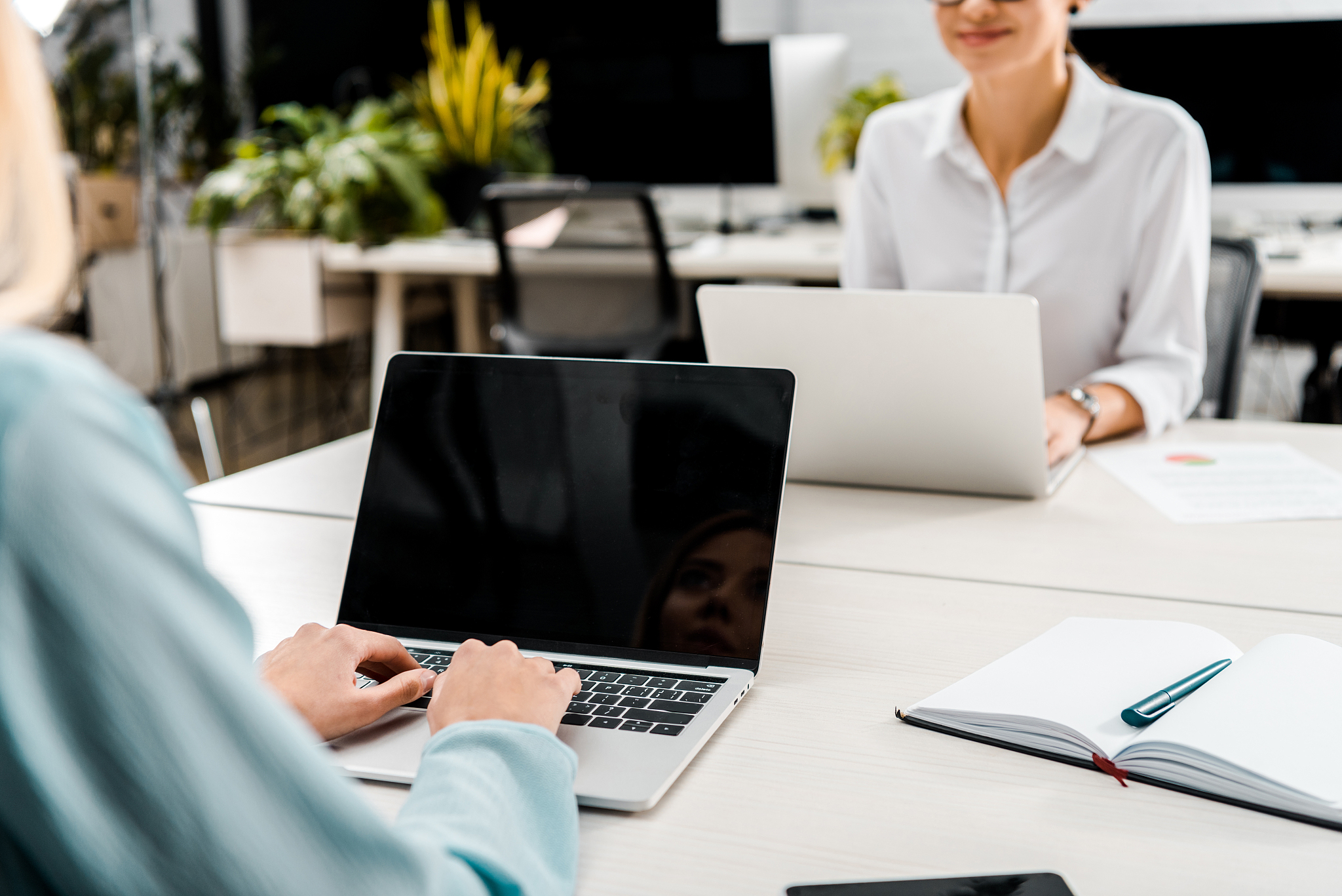 partial view of businesswomen at workplace with laptops in offic