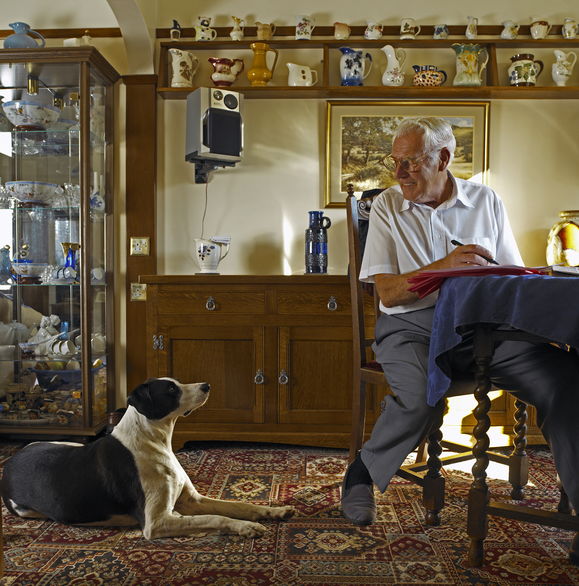 senior man at table looking down at dog, smiling