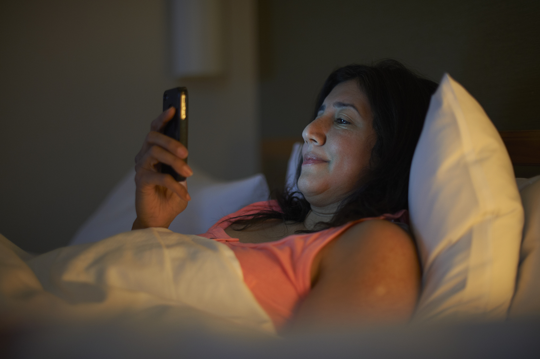 mature woman reading smartphone texts in hotel bed at night