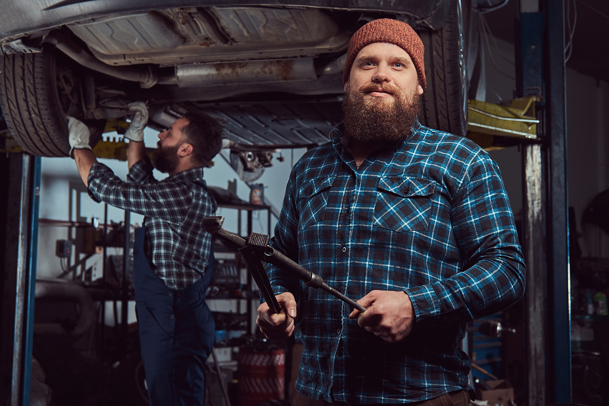 two bearded brutal mechanics repair a car on a lift in the garag