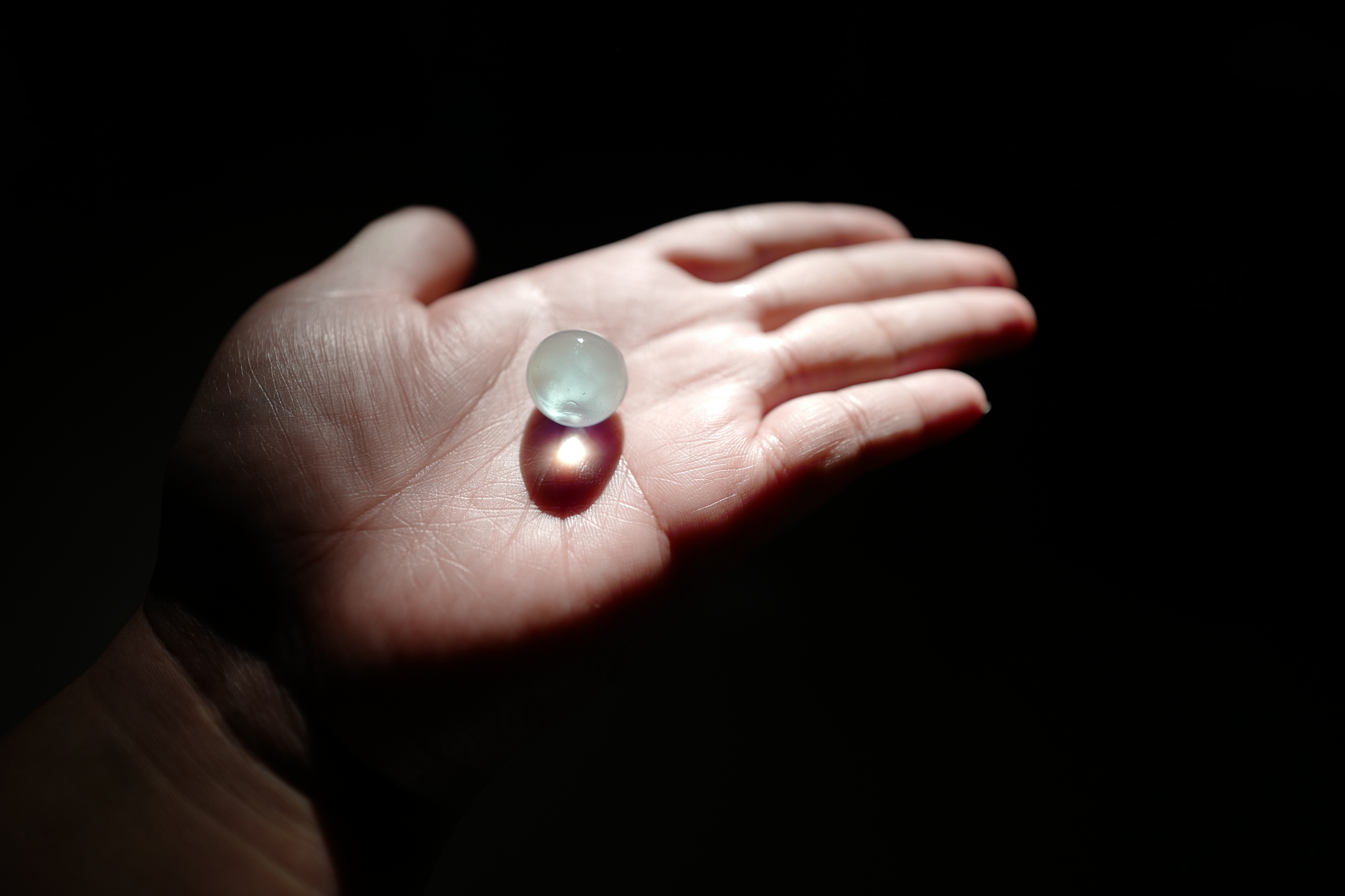 cropped hand holding marble against black background
