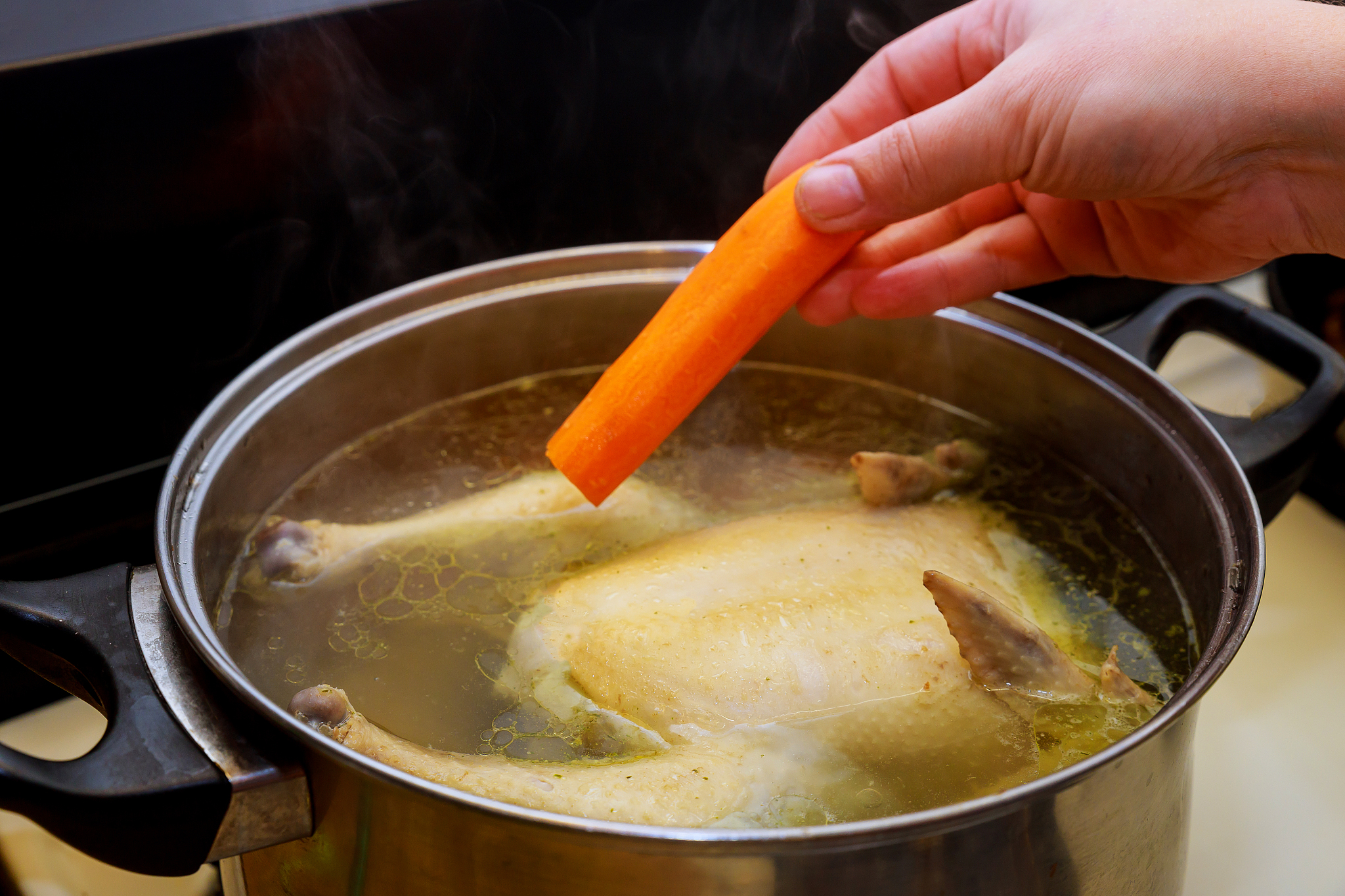 womens hand puts carrot in the chicken soup.