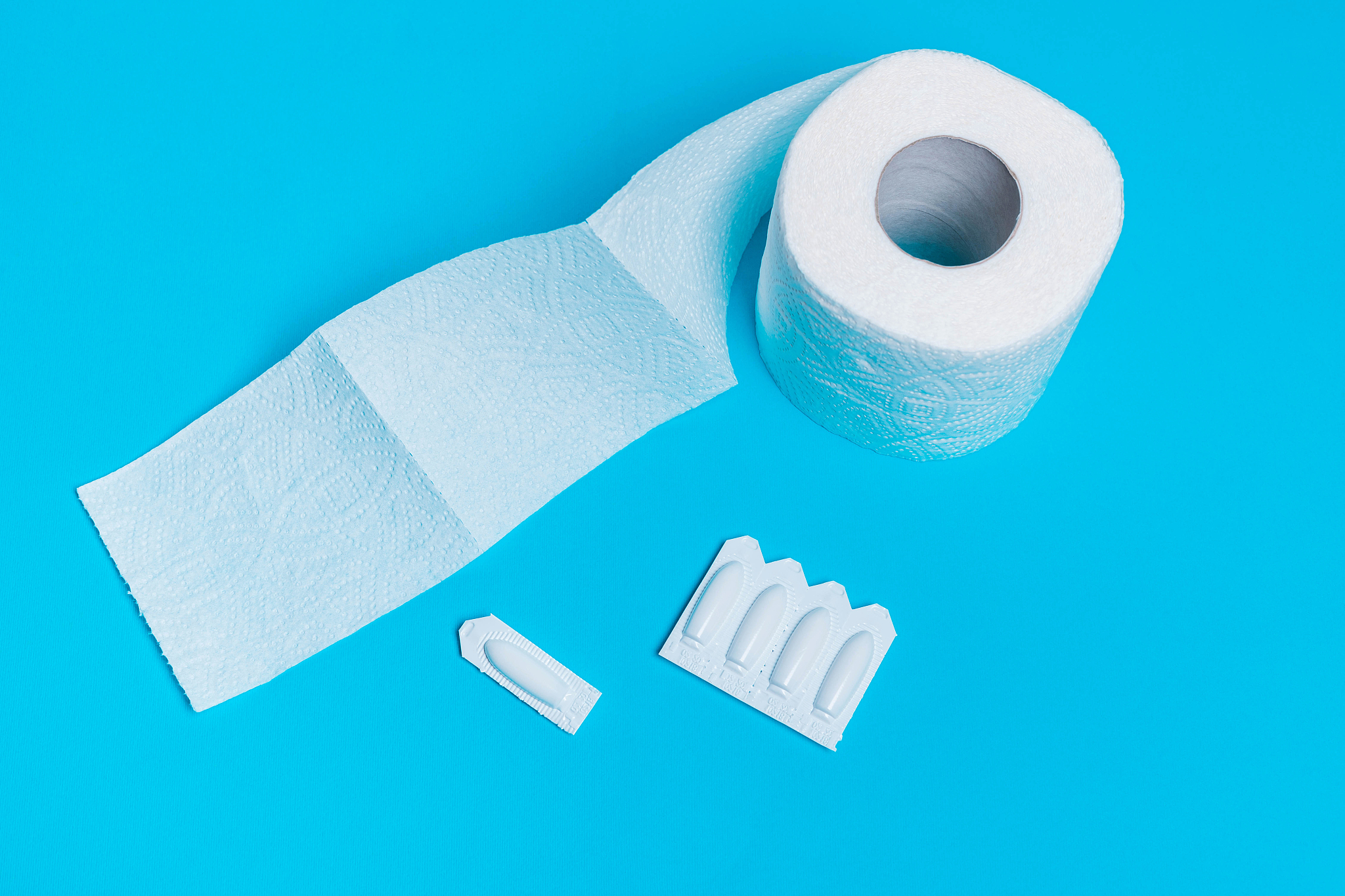 suppository and toilet paper on a blue background, for the treat