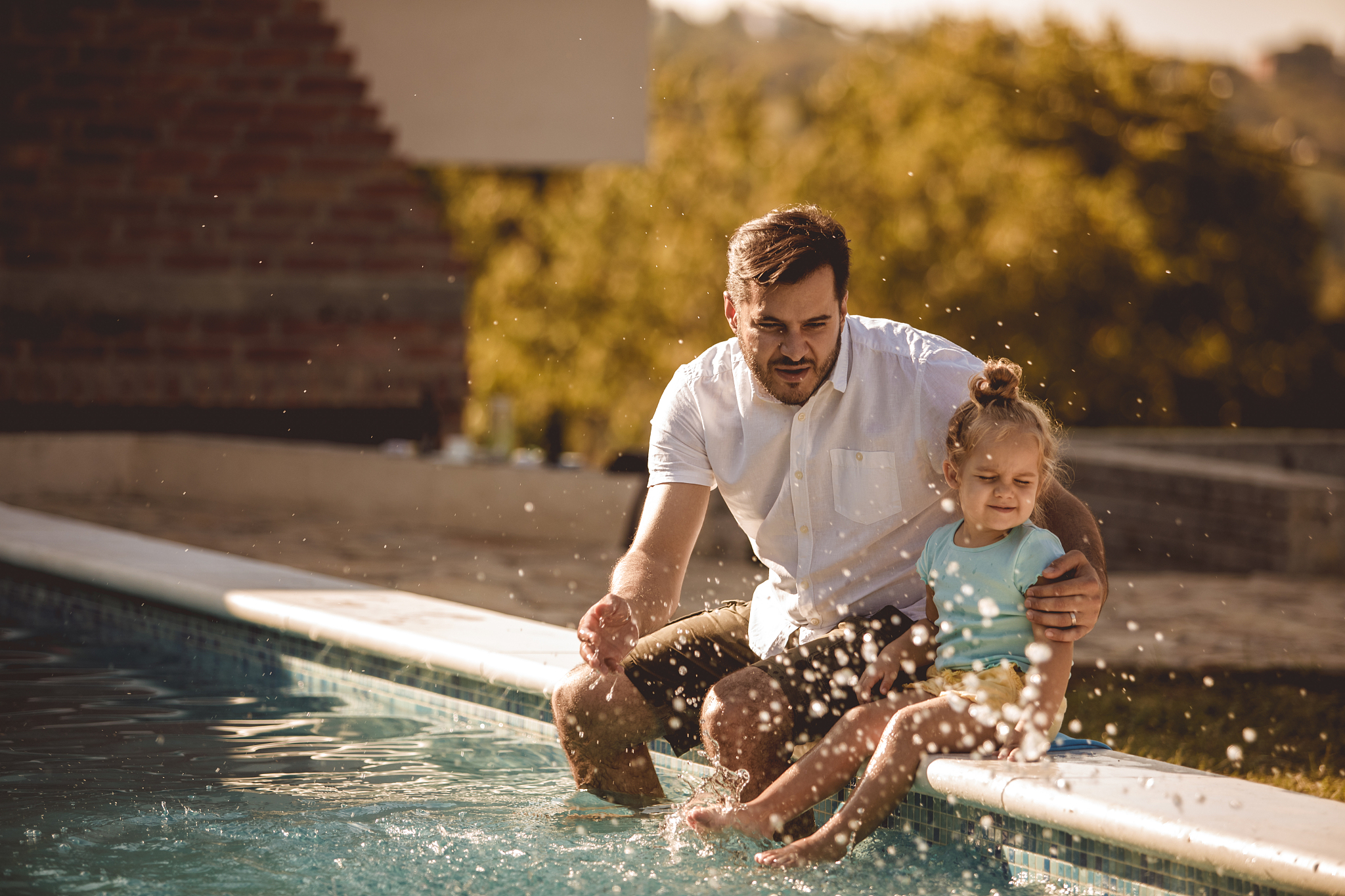 father and daughter splashing the water in the swimming pool