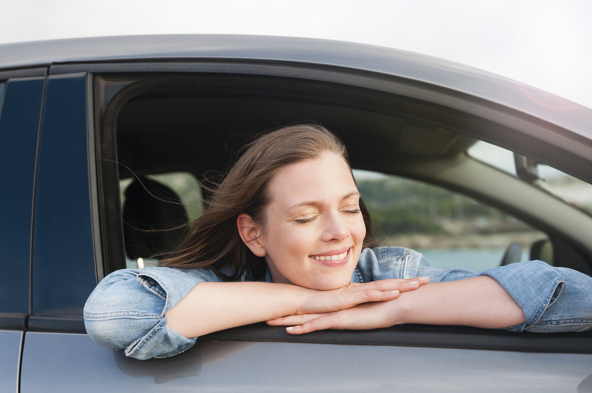 portrait of smling woman with eyes closed leaning out of car won
