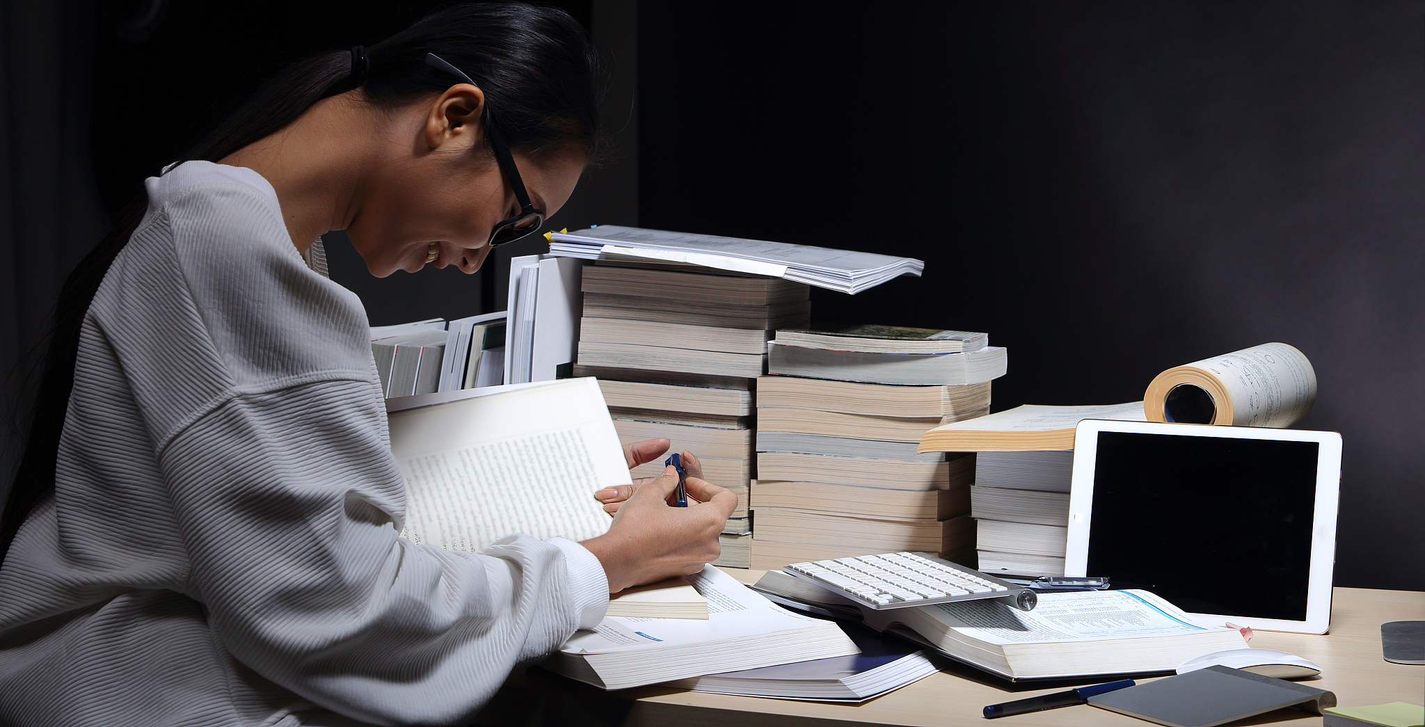 girl in white shirt reading many textbooks on table with many hi