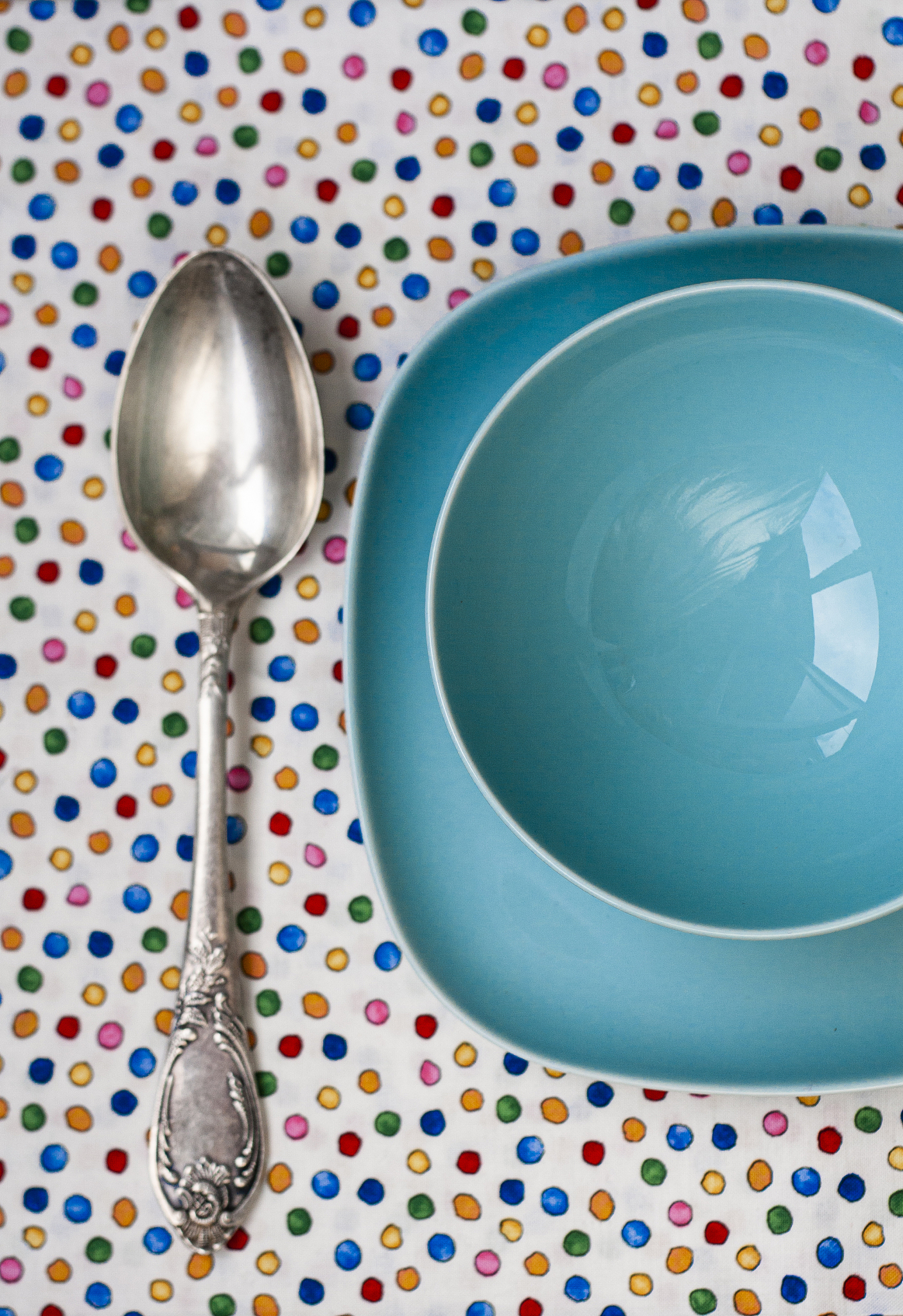 a large spoon rests on a tablecloth next to two blue plates.