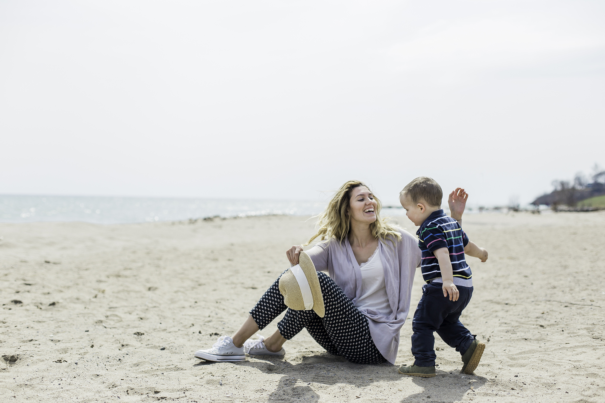 young woman sitting on beach playing with toddler son