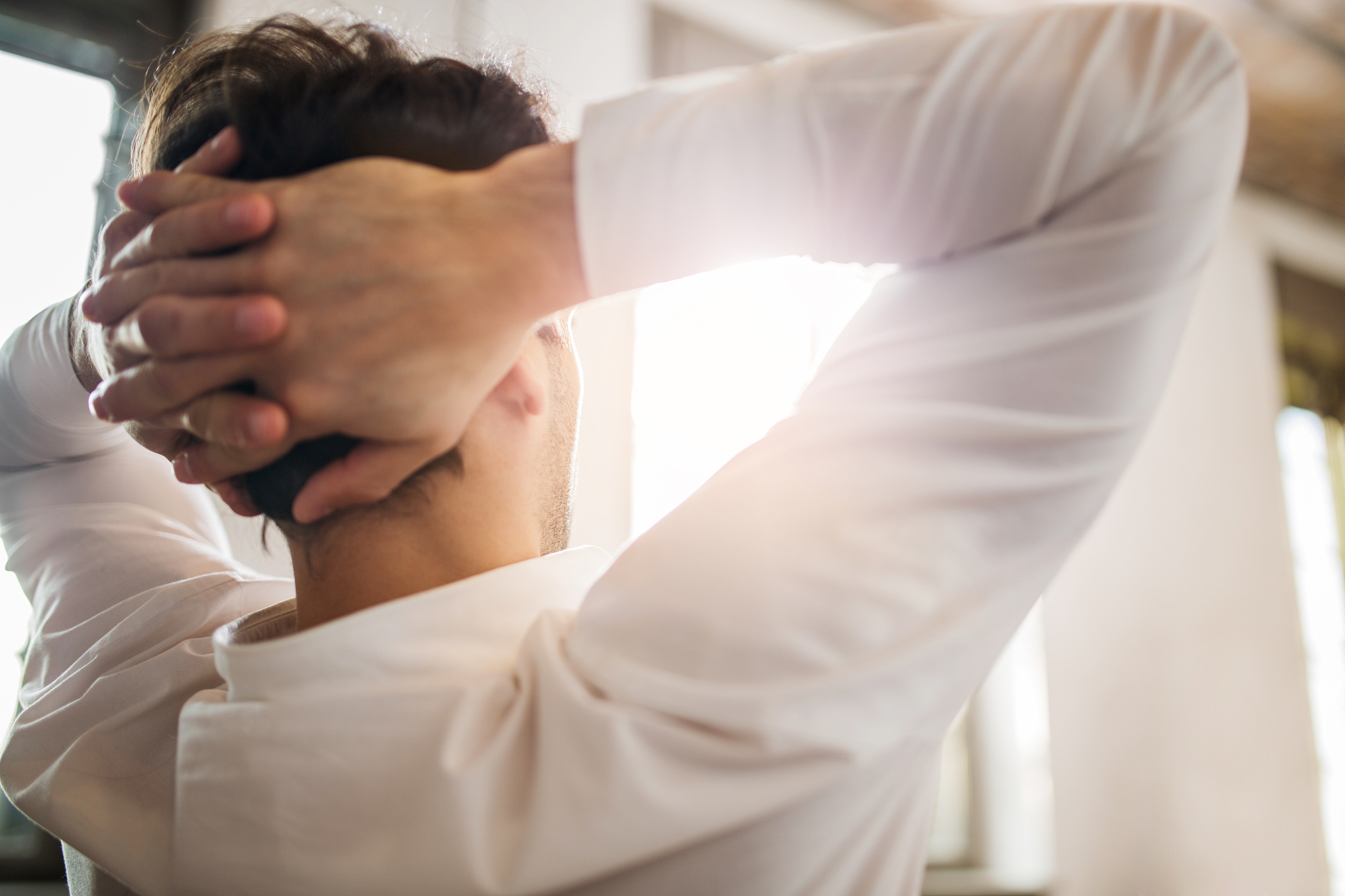 close up of a man with hands behind his head.