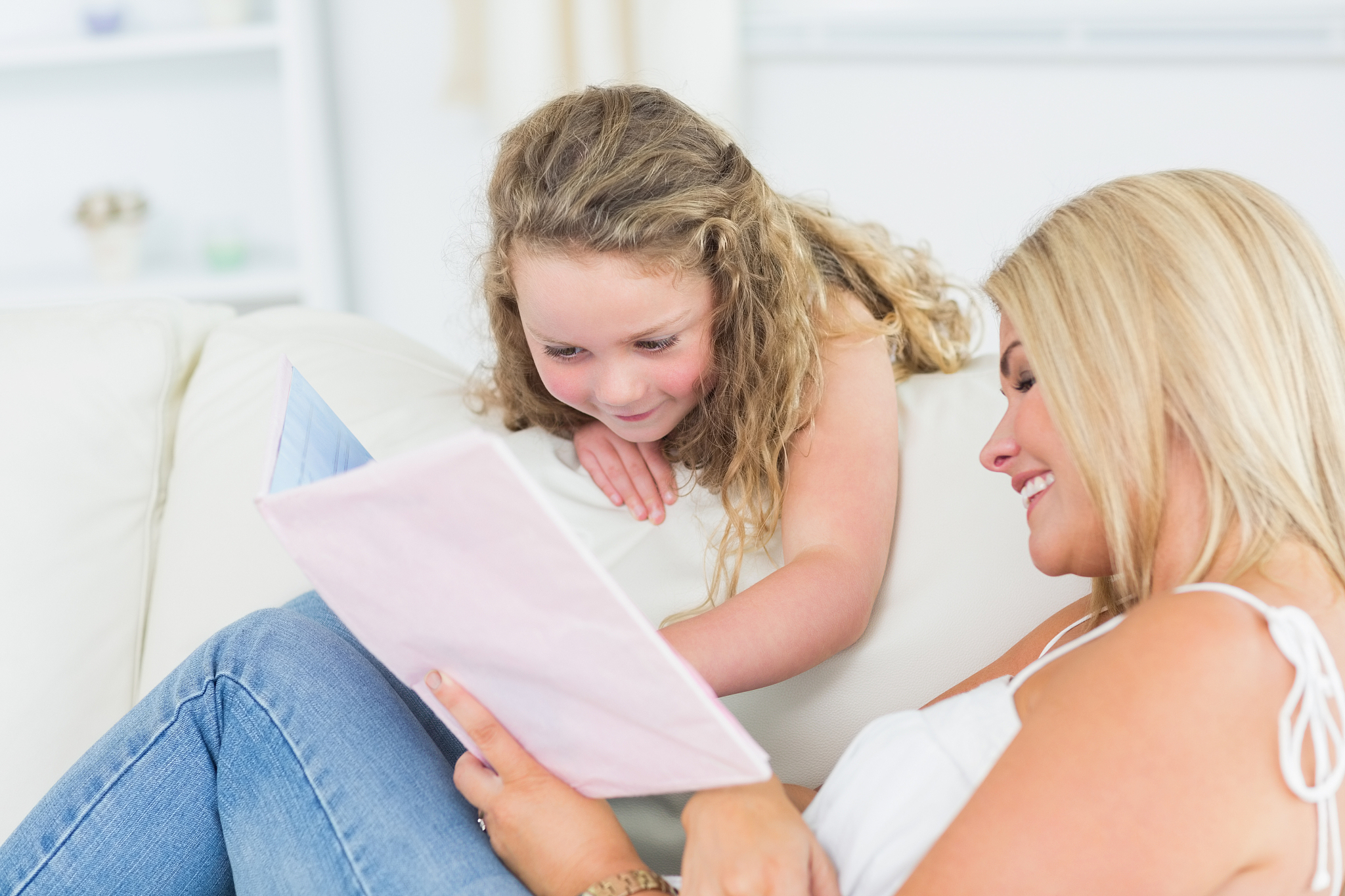 mother showing something to her daughter in book on the couch