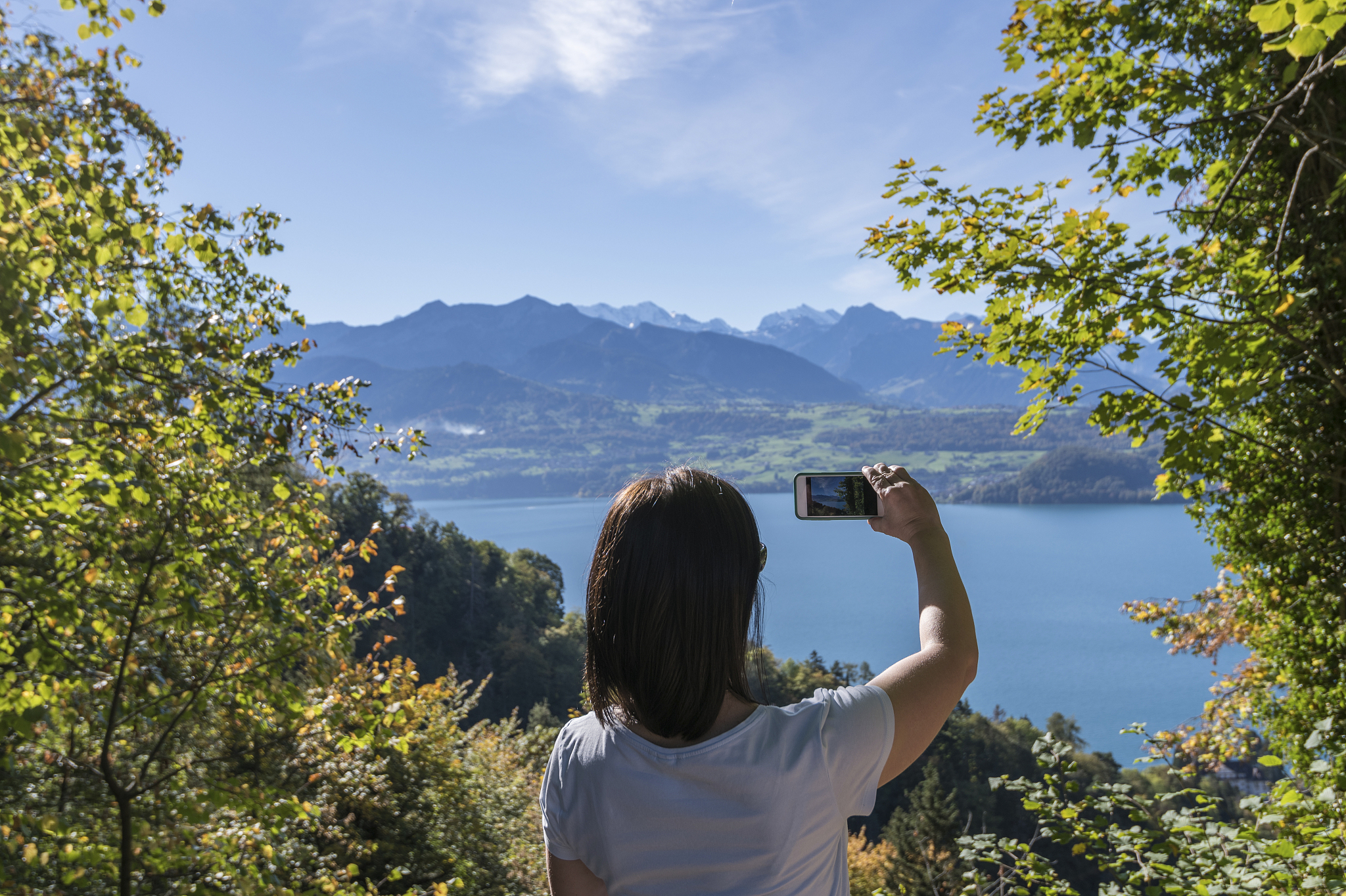 woman pauses in front of lake, takes pic of view