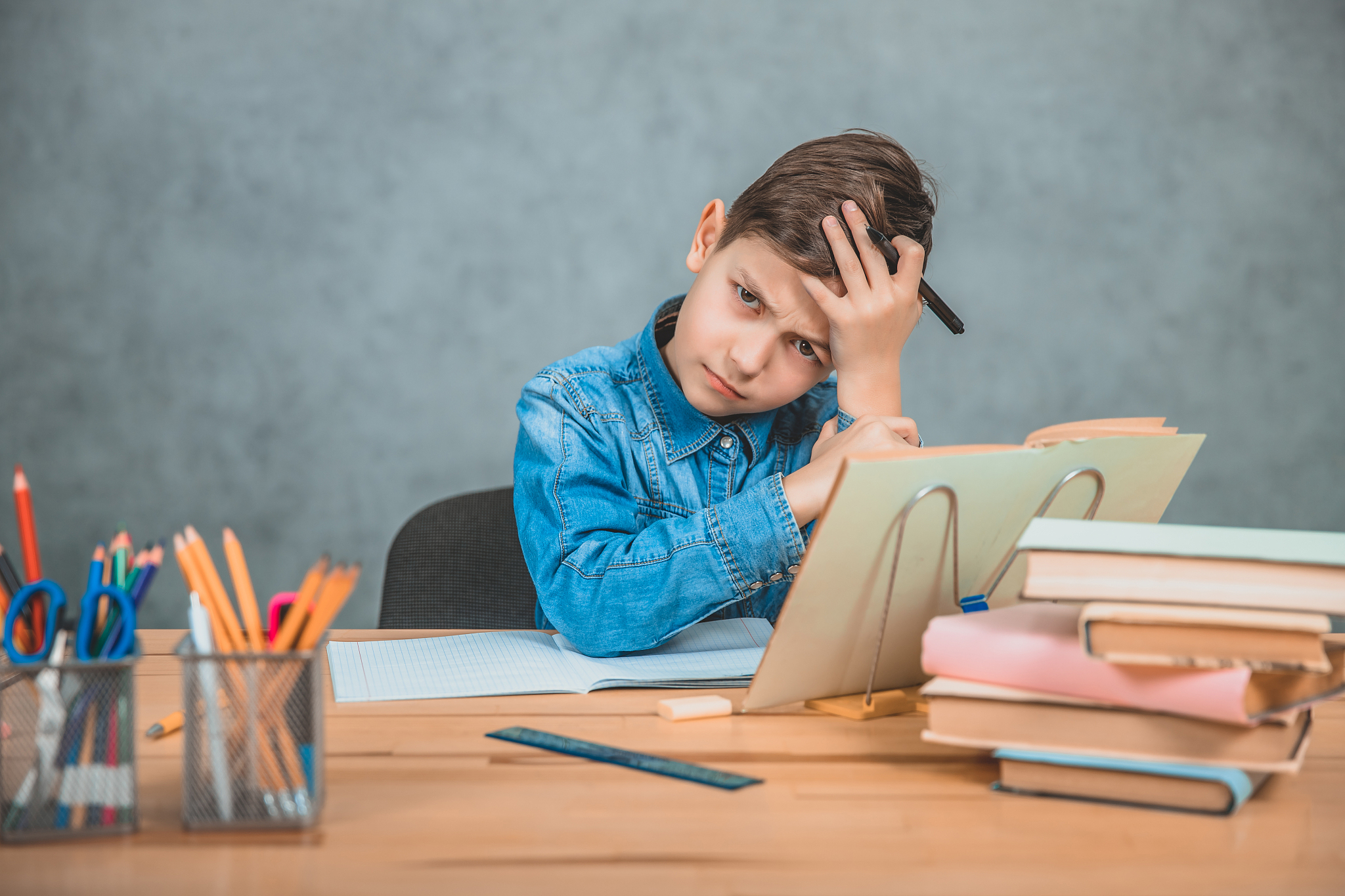 little tired schoolboy is sitting at the desk, holding hand on t