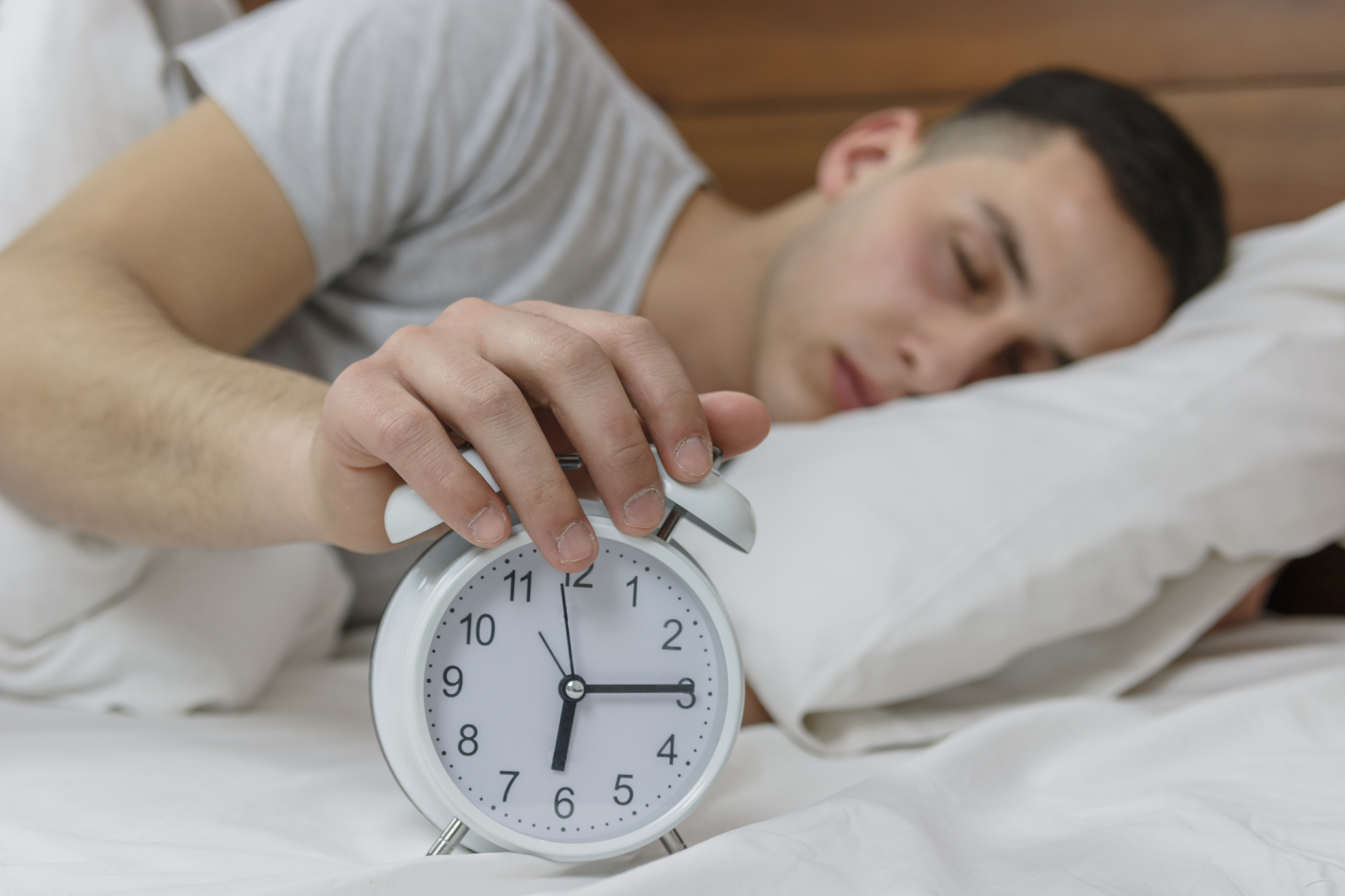 young sleepy man trying to turns off the alarm clock waking up a