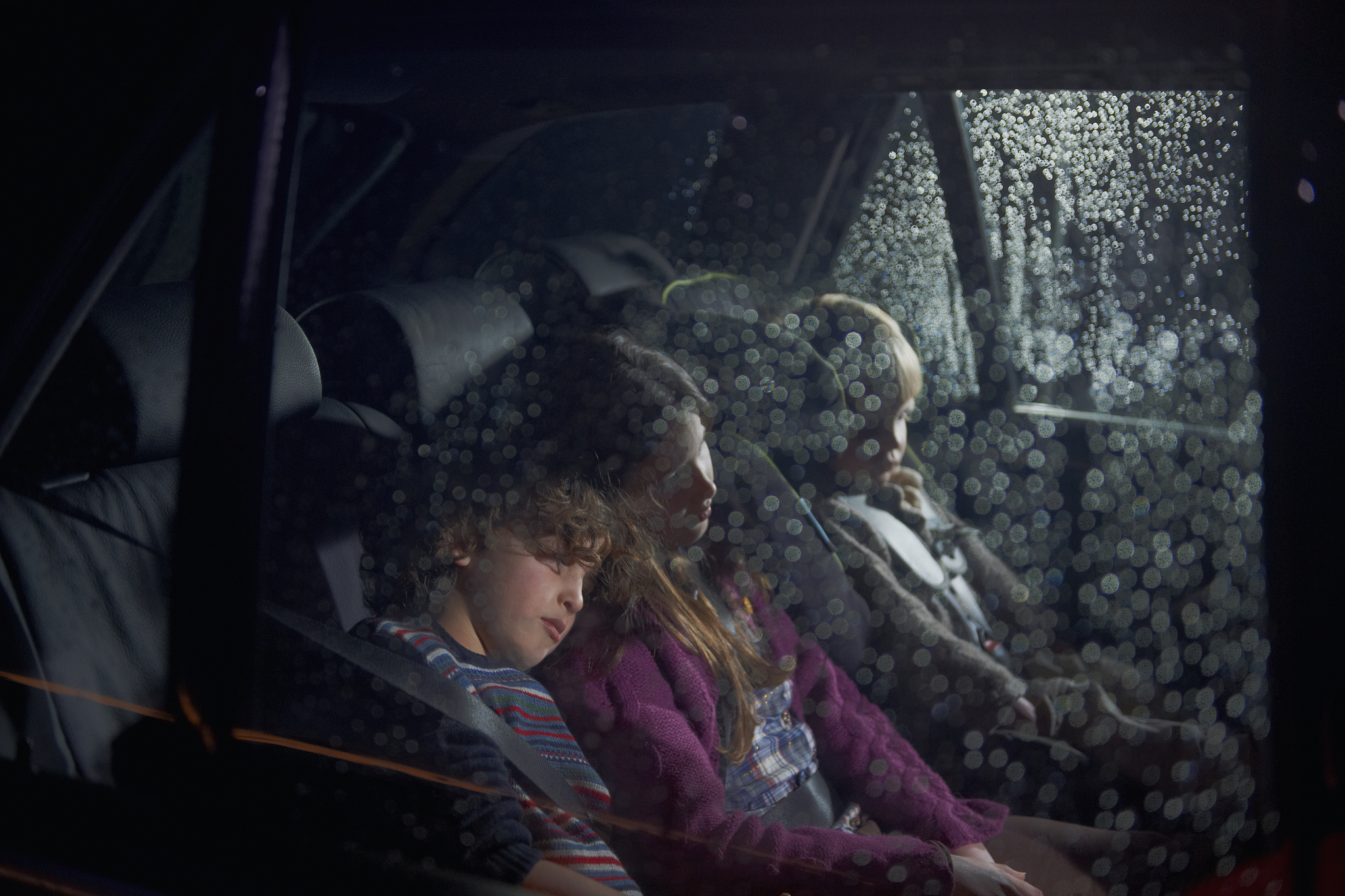three children asleep in the rear seat of a car