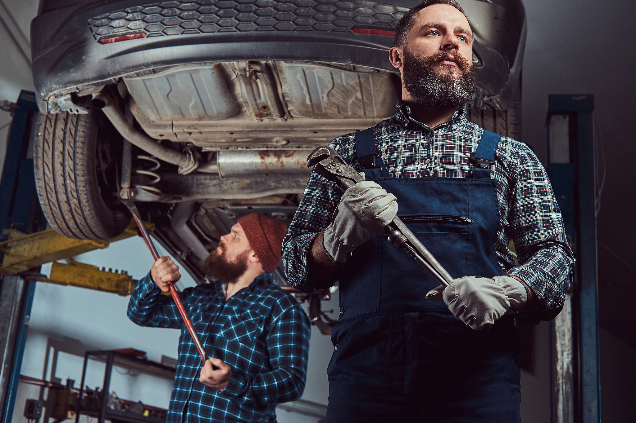two bearded brutal mechanics repair a car on a lift in a garage.