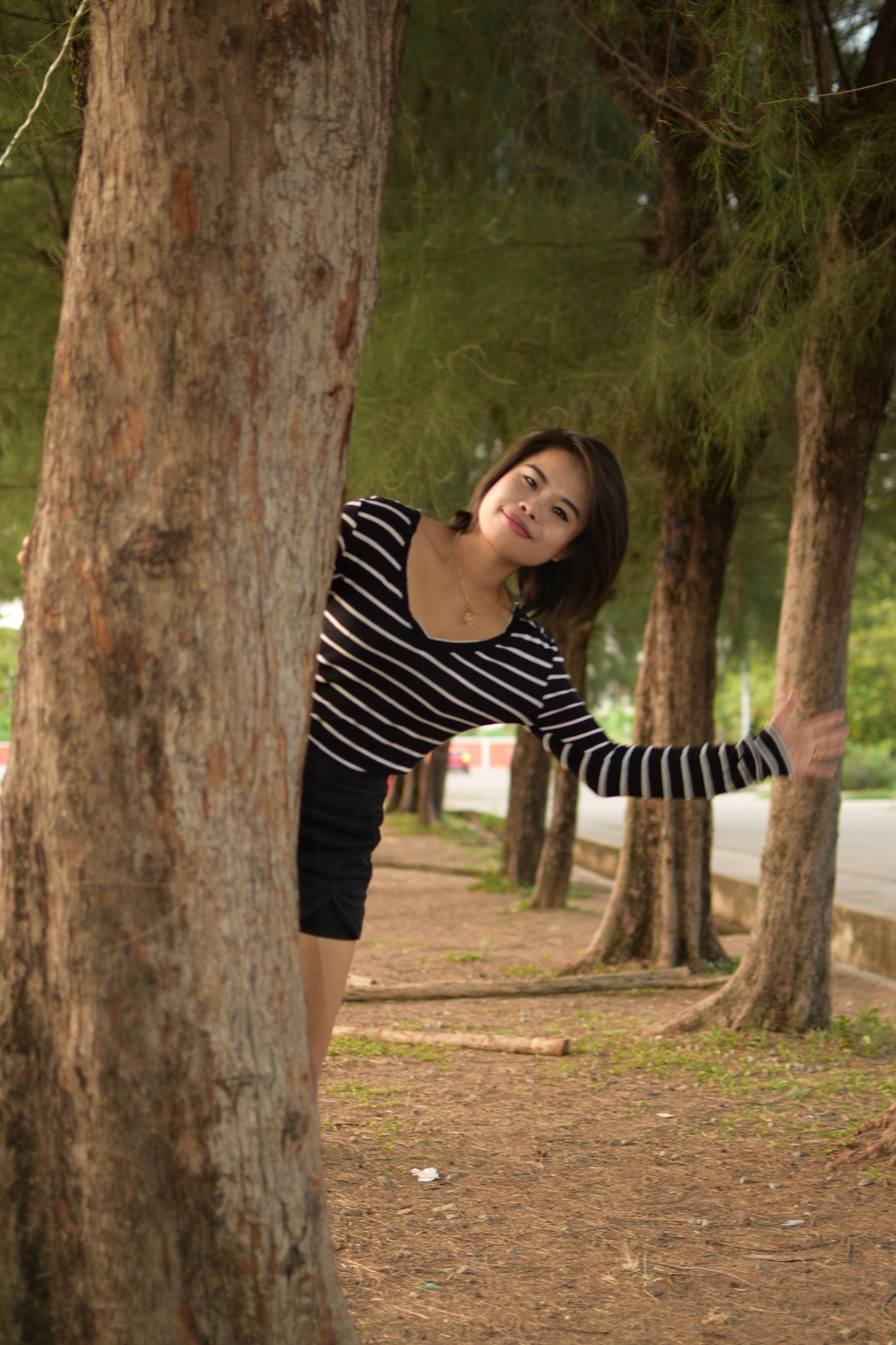 portrait of beautiful young woman standing by tree trunk in park