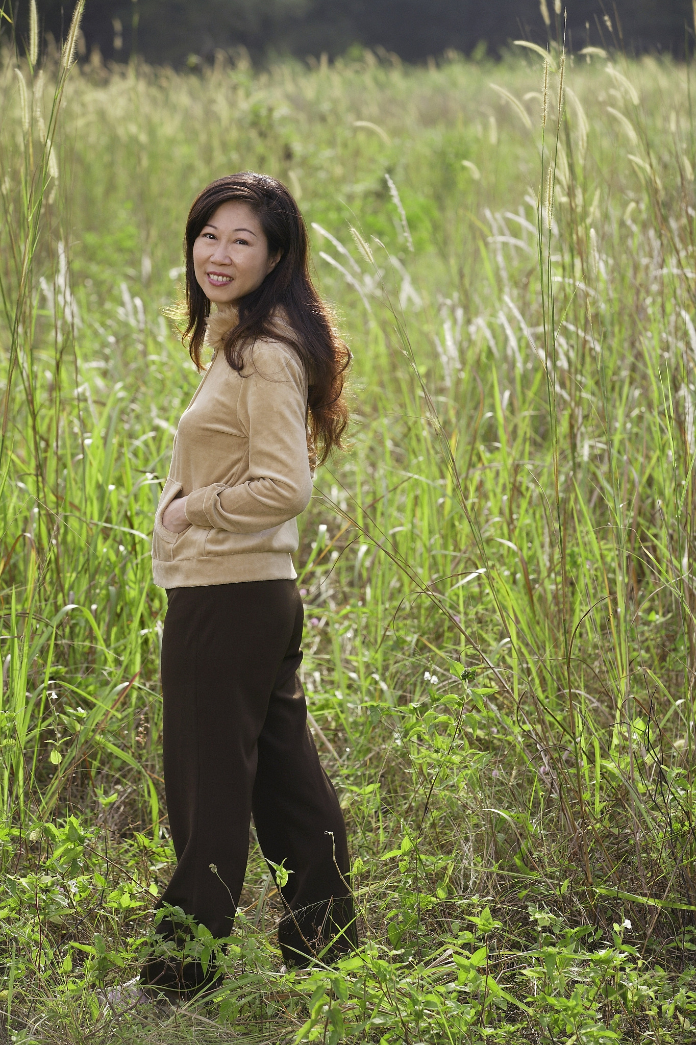woman standing in tall grass,looking over shoulder at camera