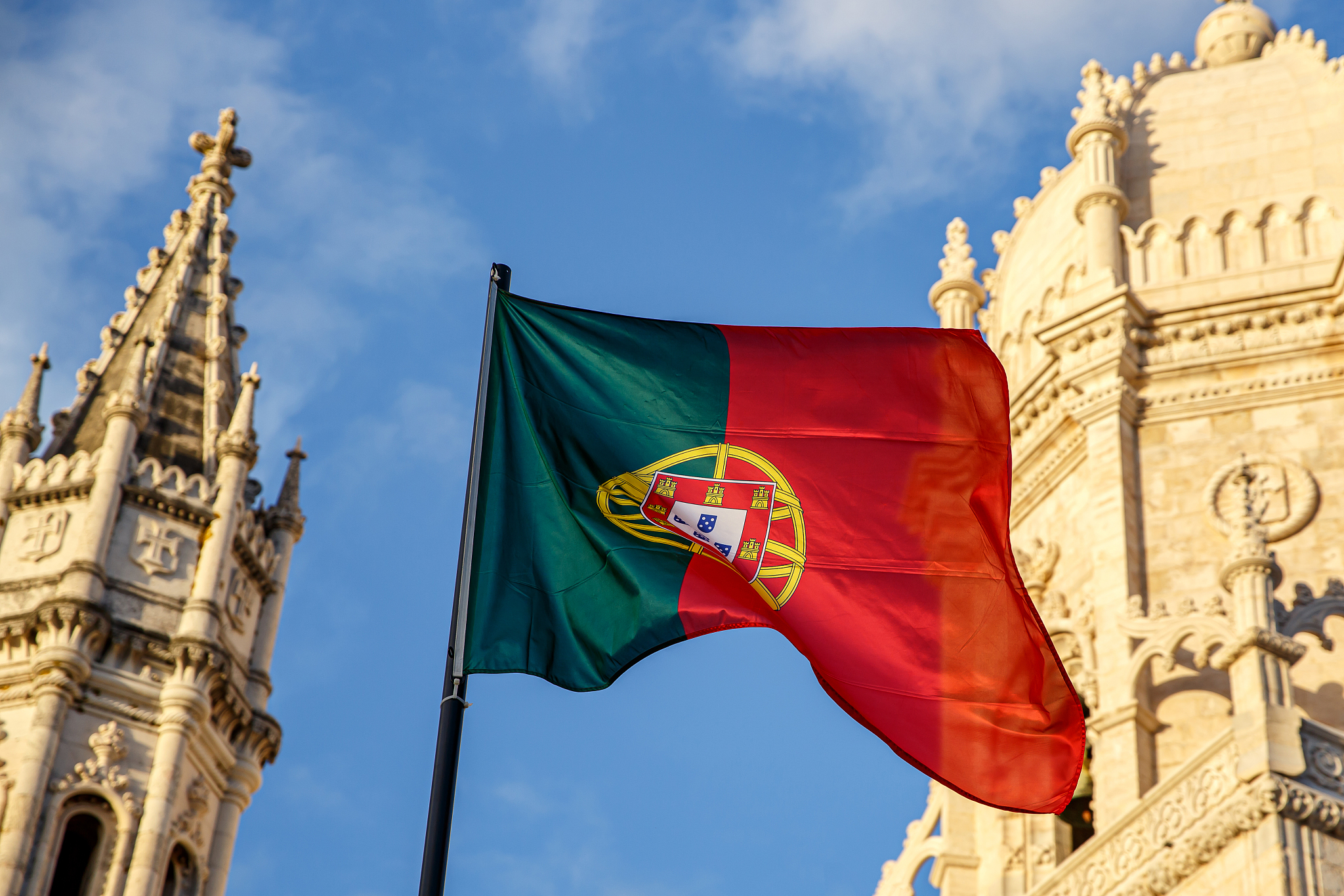 portuguese flag waving in front of a blue sky and monastery.