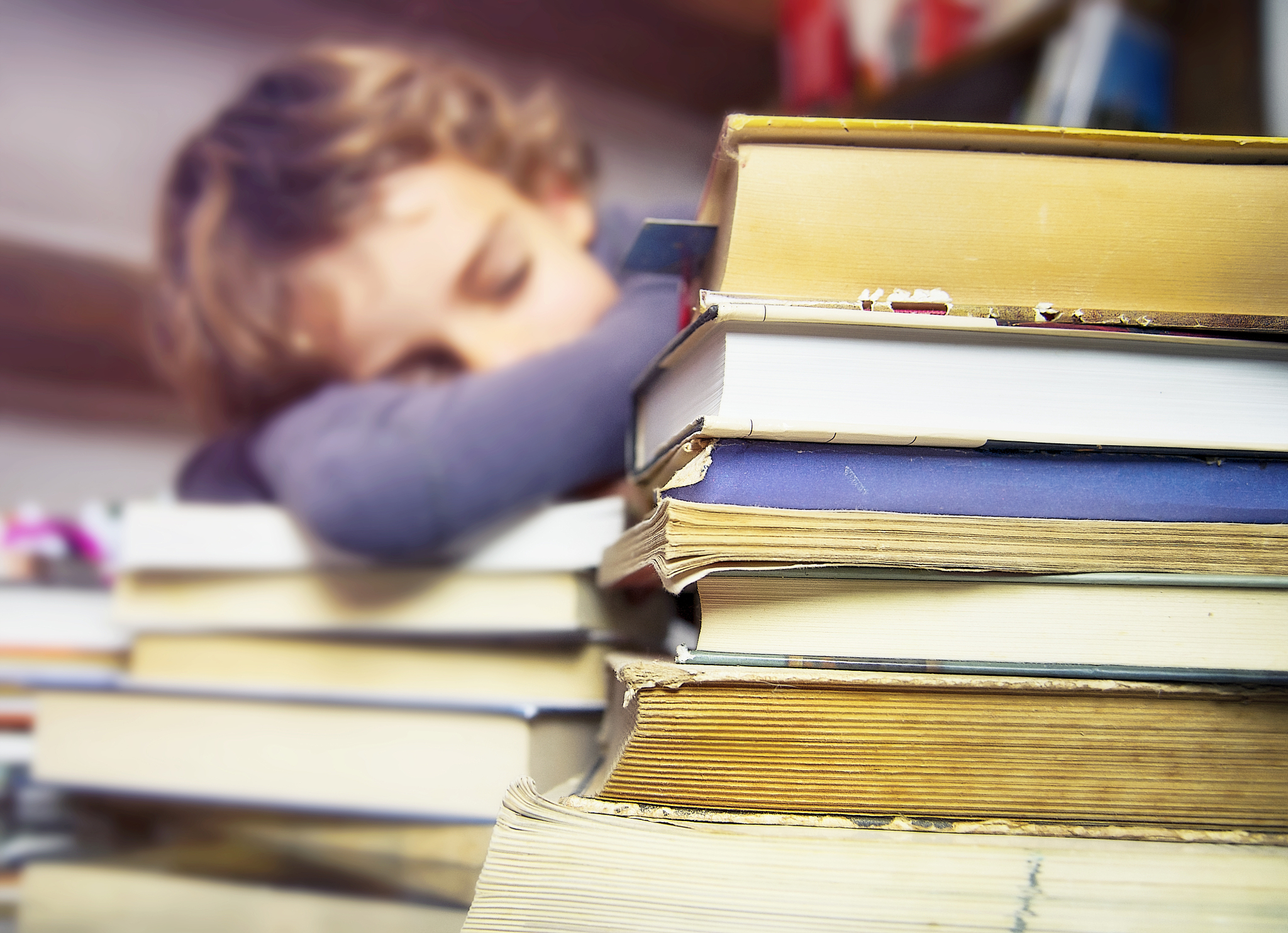 tired boy sleeps on the table full of books