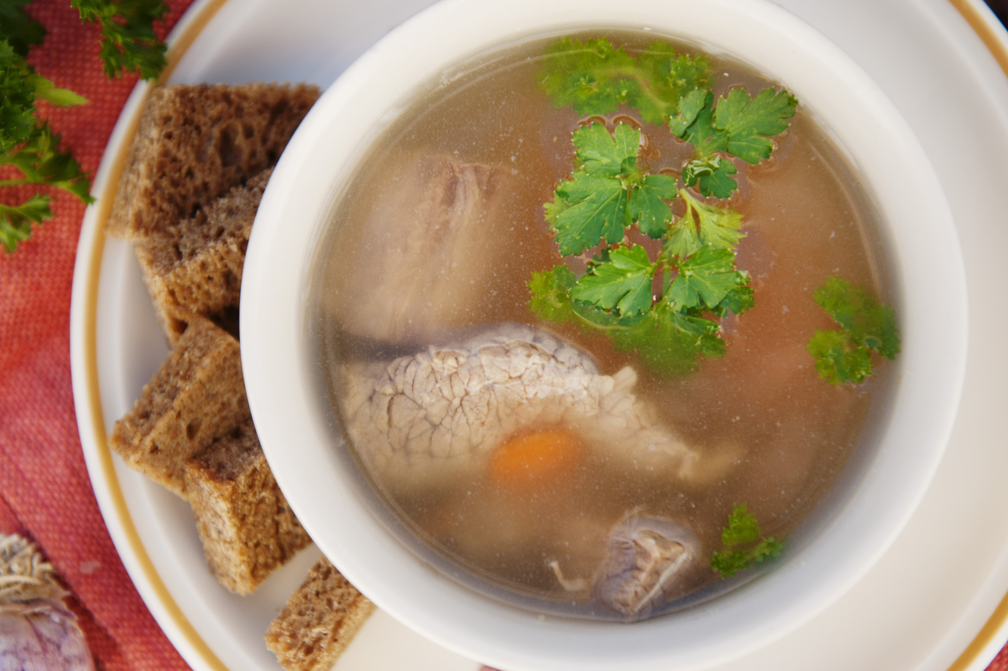 clear beef broth, bouillon in white bowl and vegetables on woode