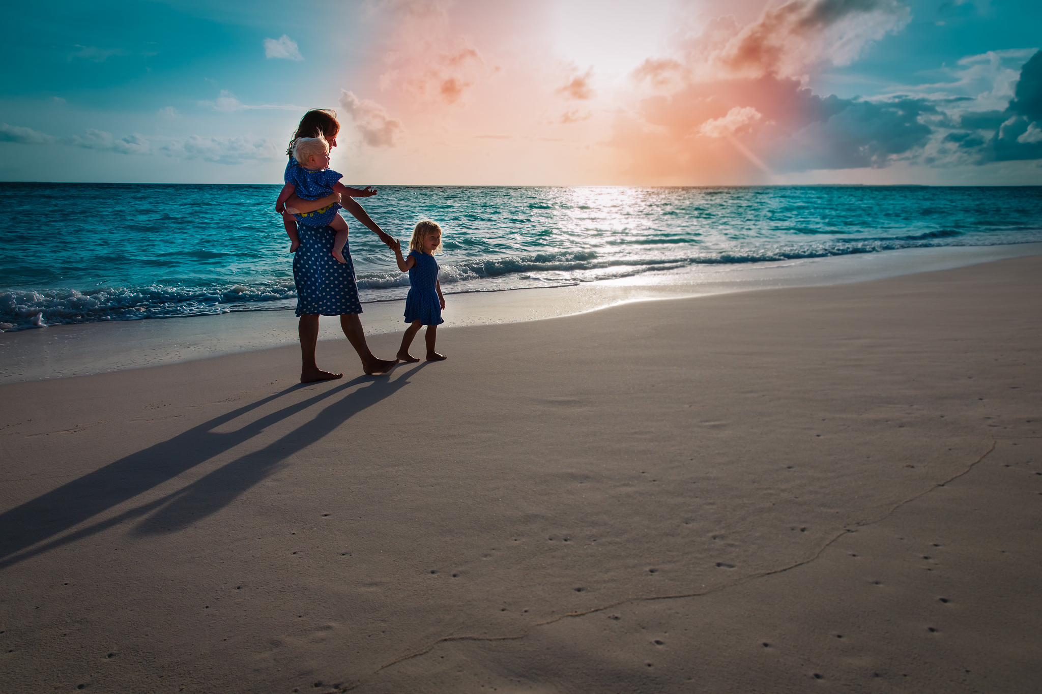 mother with kids walk on sunset beach