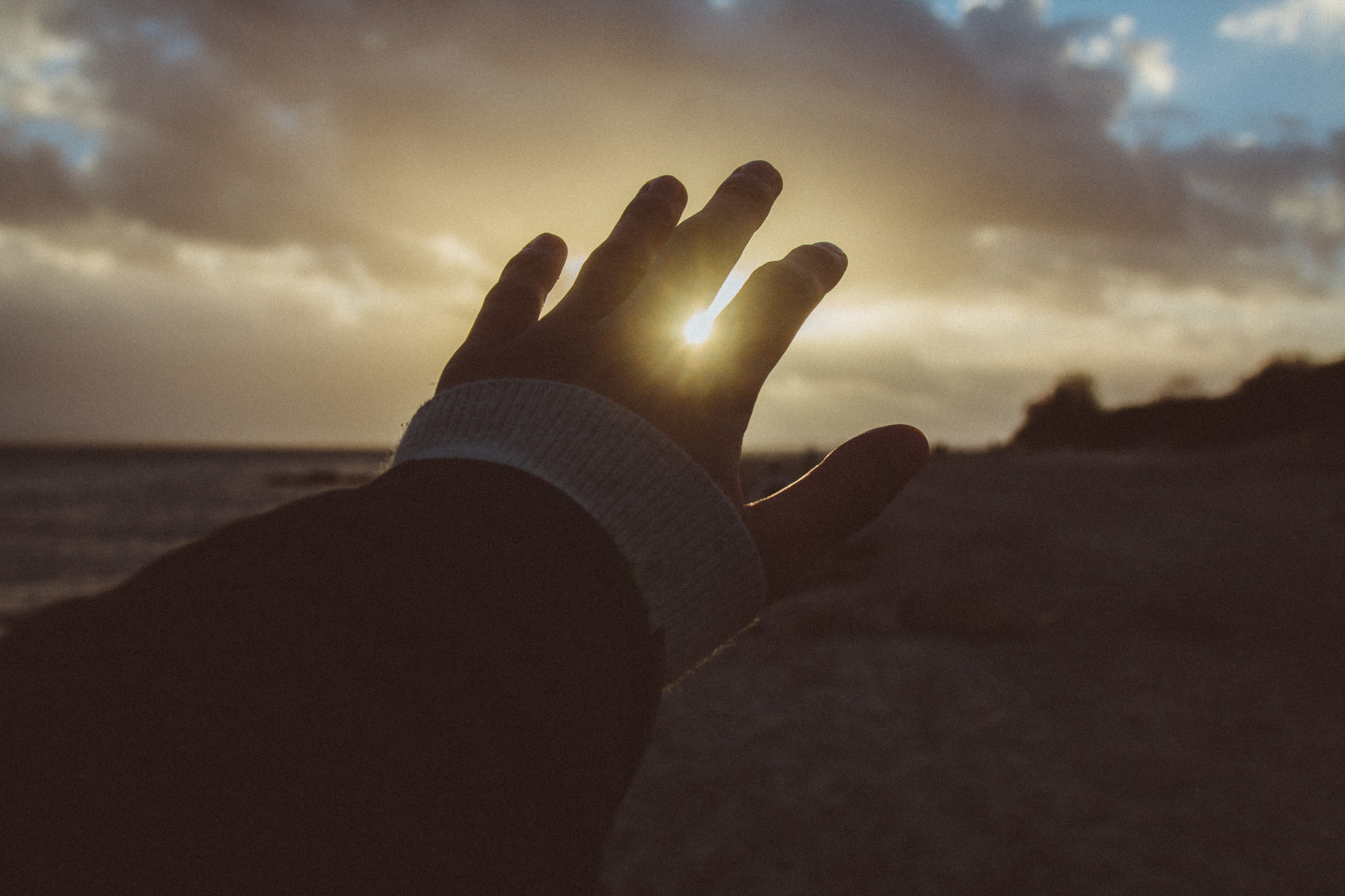 cropped hand of person gesturing at beach against sky during sun