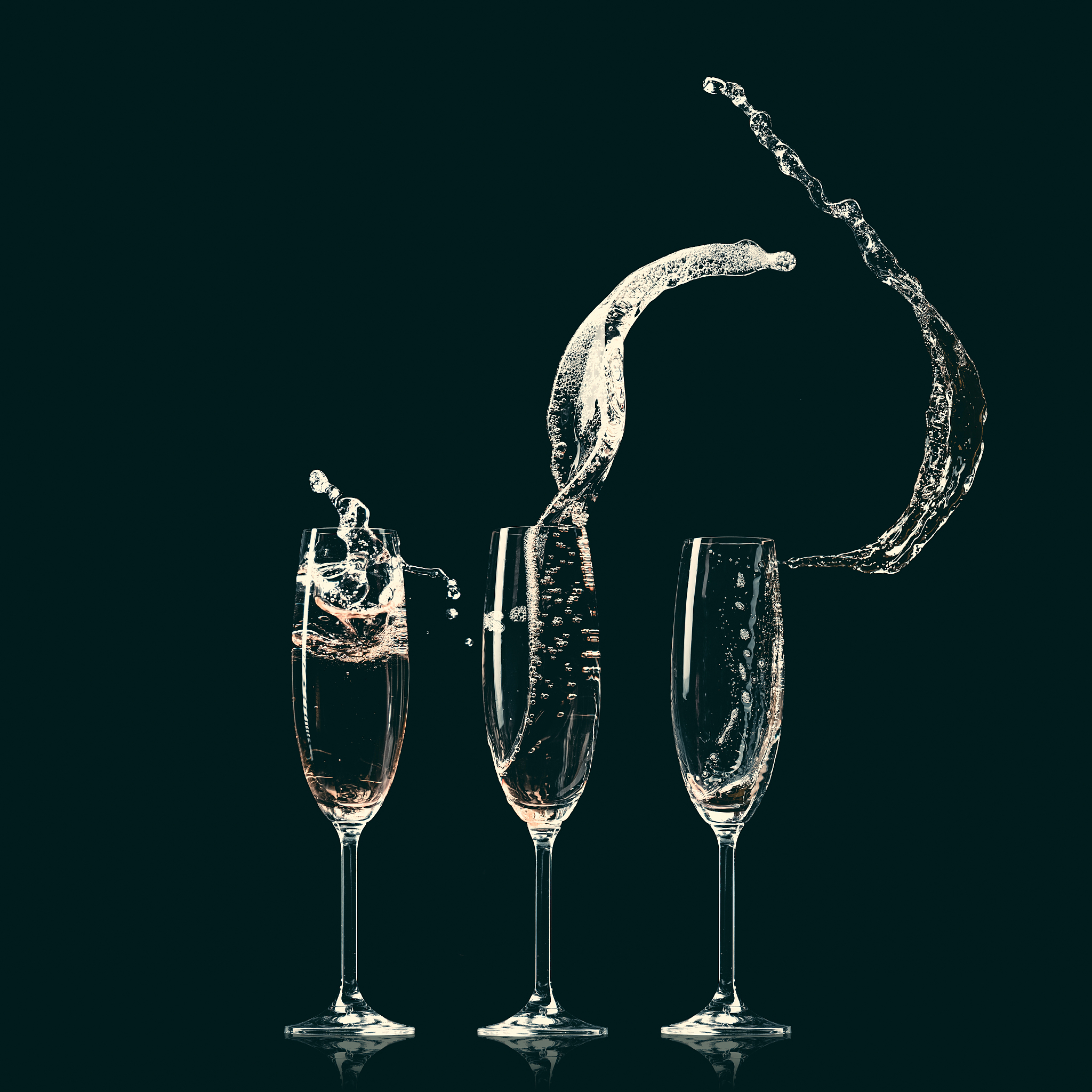 three glasses with splashes of champagne on black