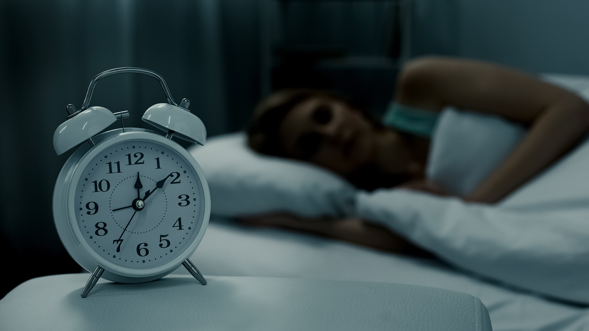 young lady resting in her bed, midnight time shown on alarm cloc