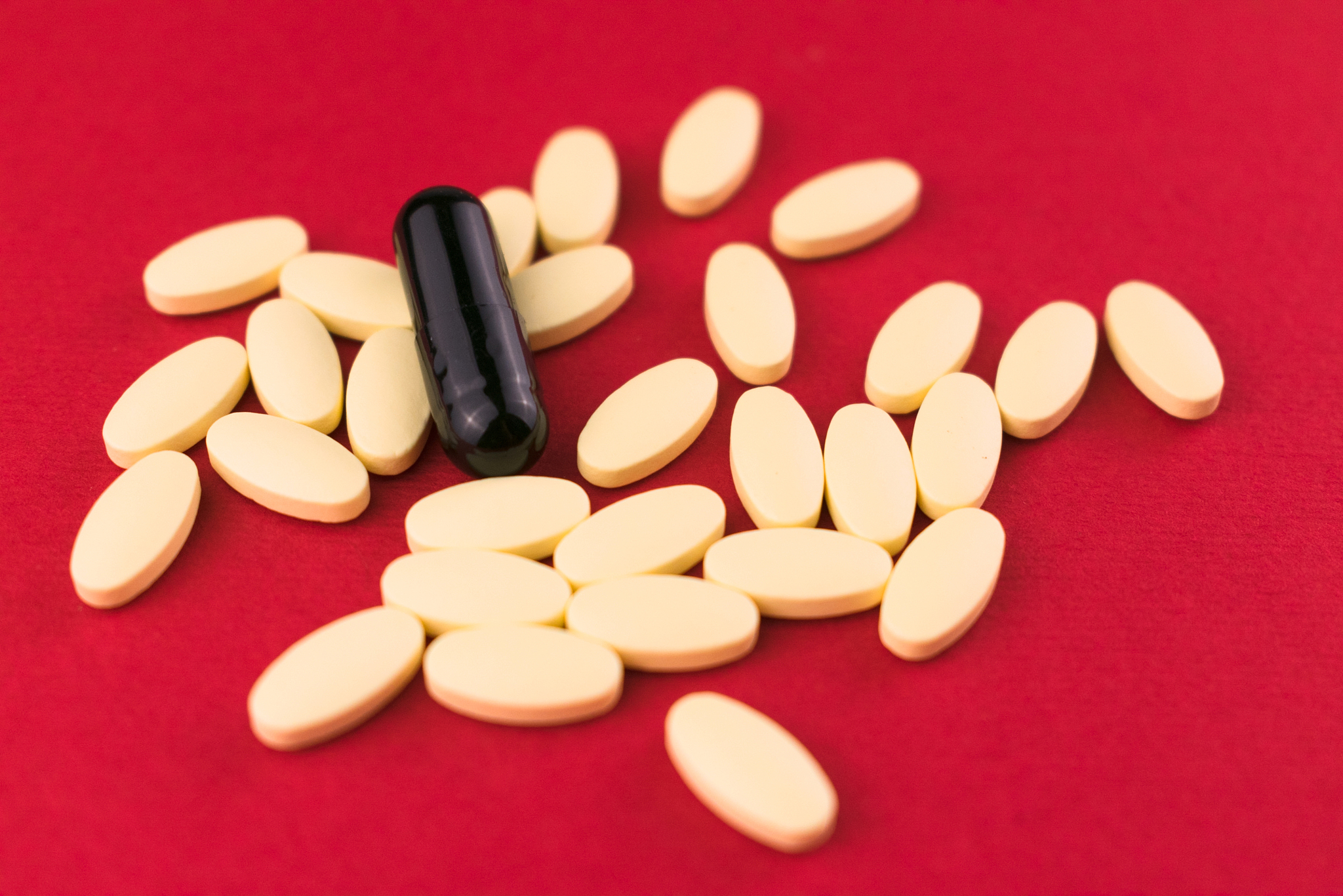 white pills and one black capsule on a red background.